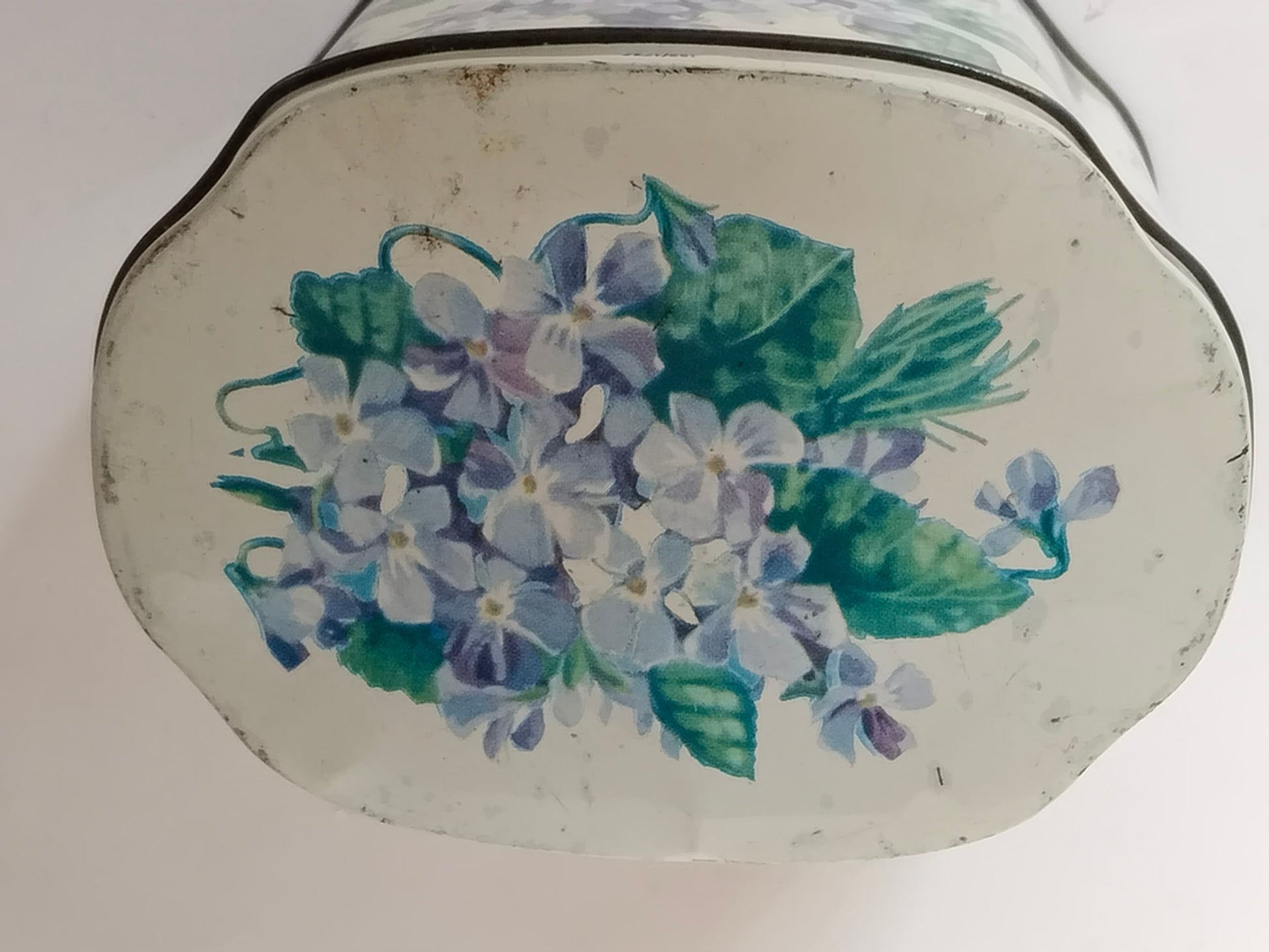 Seitliches Detail der ovalen Blechdose mit Veilchen und grünen Blättern
