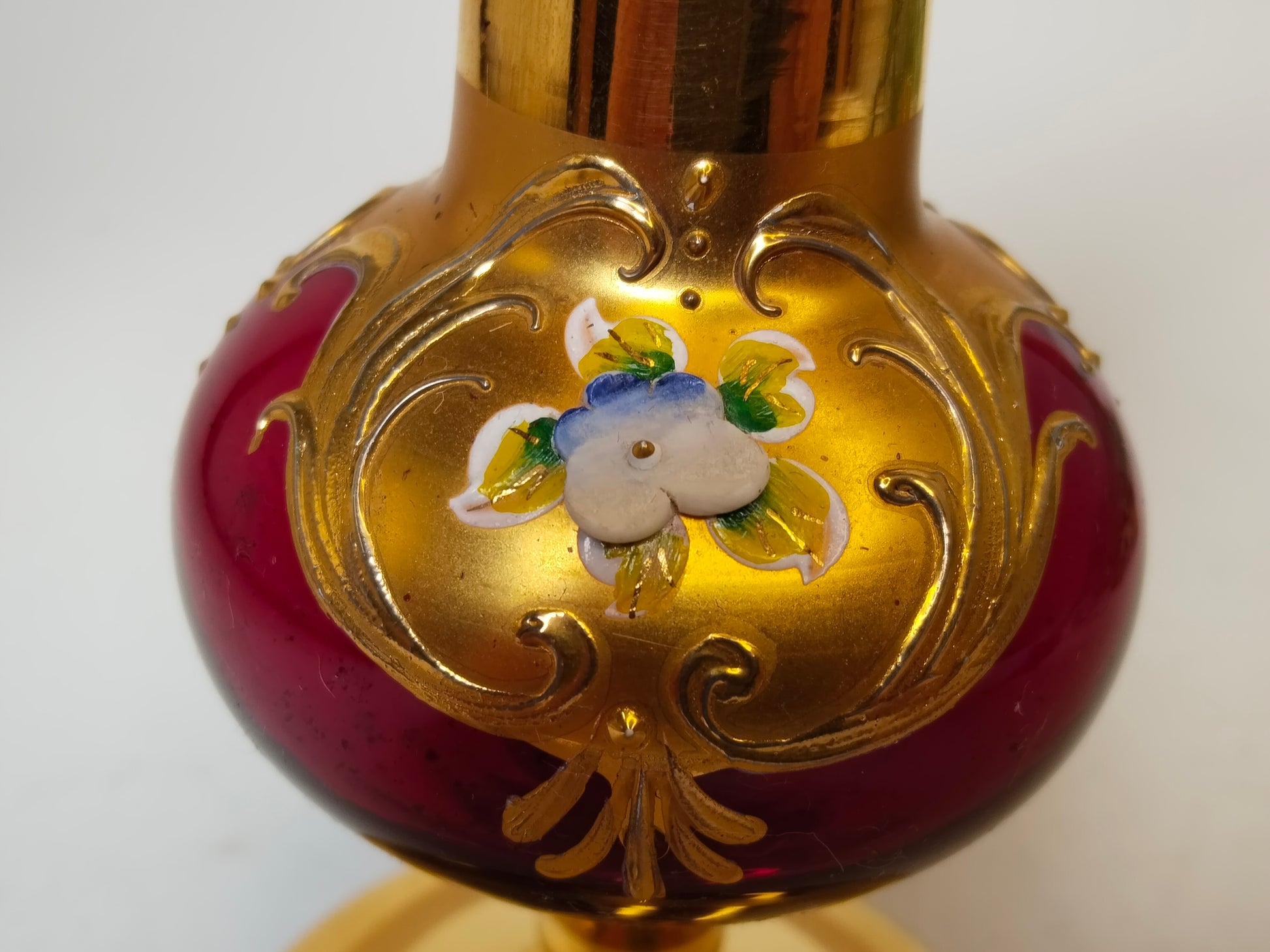 Detailaufnahme Bauch der Vase, erhabenes Gold-Rankwerk und Emaille-Blüte auf Weinrot

