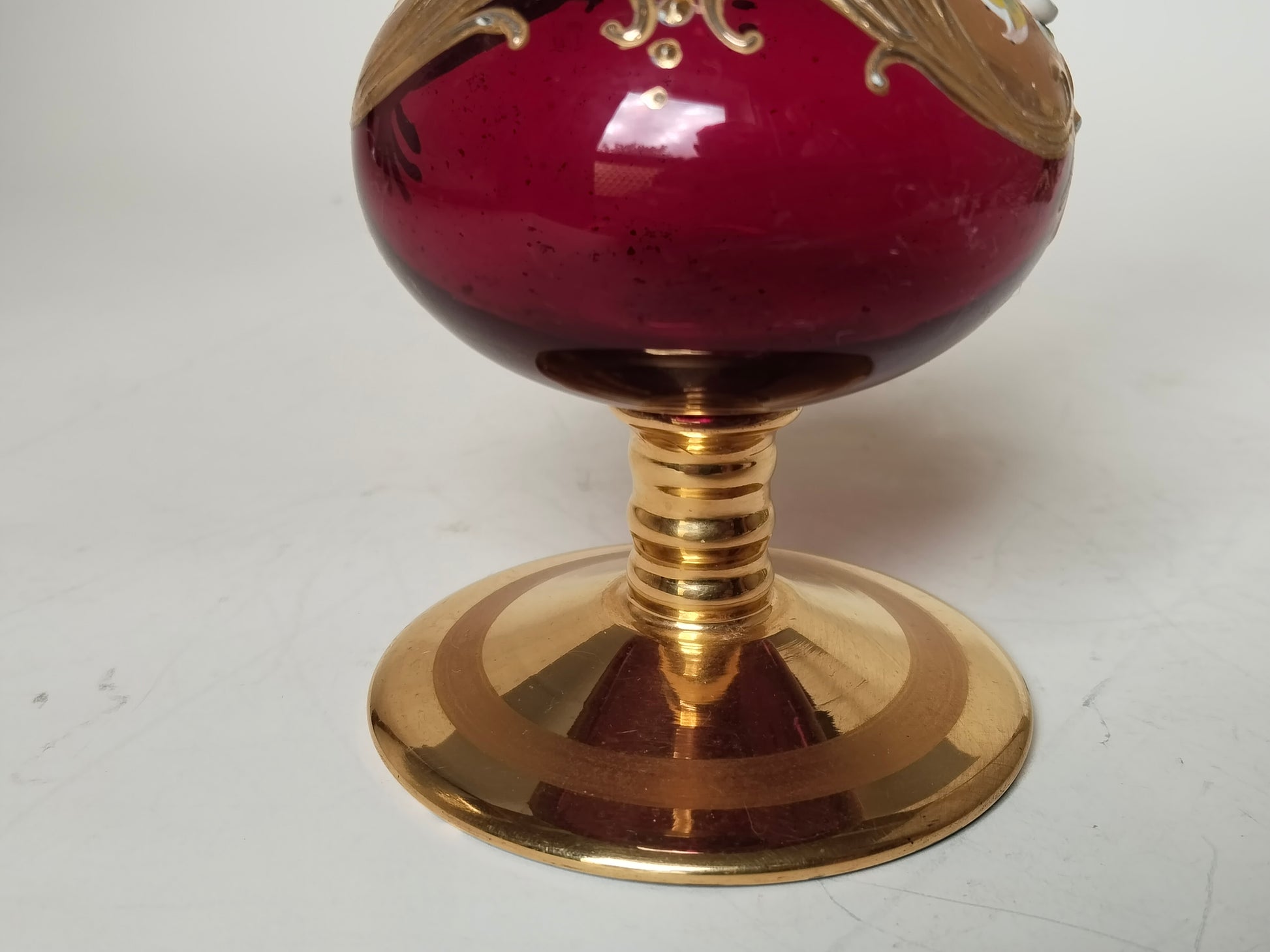 Detail des weinroten Glasbauchs mit Goldornament und geripptem Goldfuß
