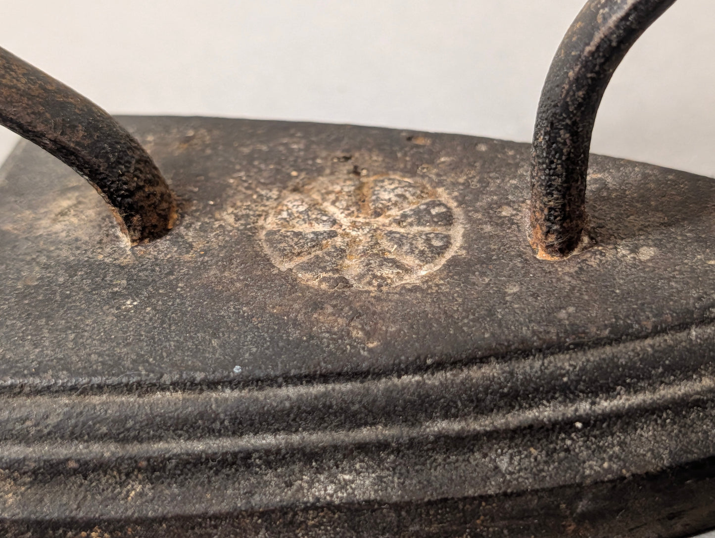Detailaufnahme der Rosetten-Gussmarke auf dem antiken Bügeleisen, gerippter Zierrand, Gusseisen mit Patina