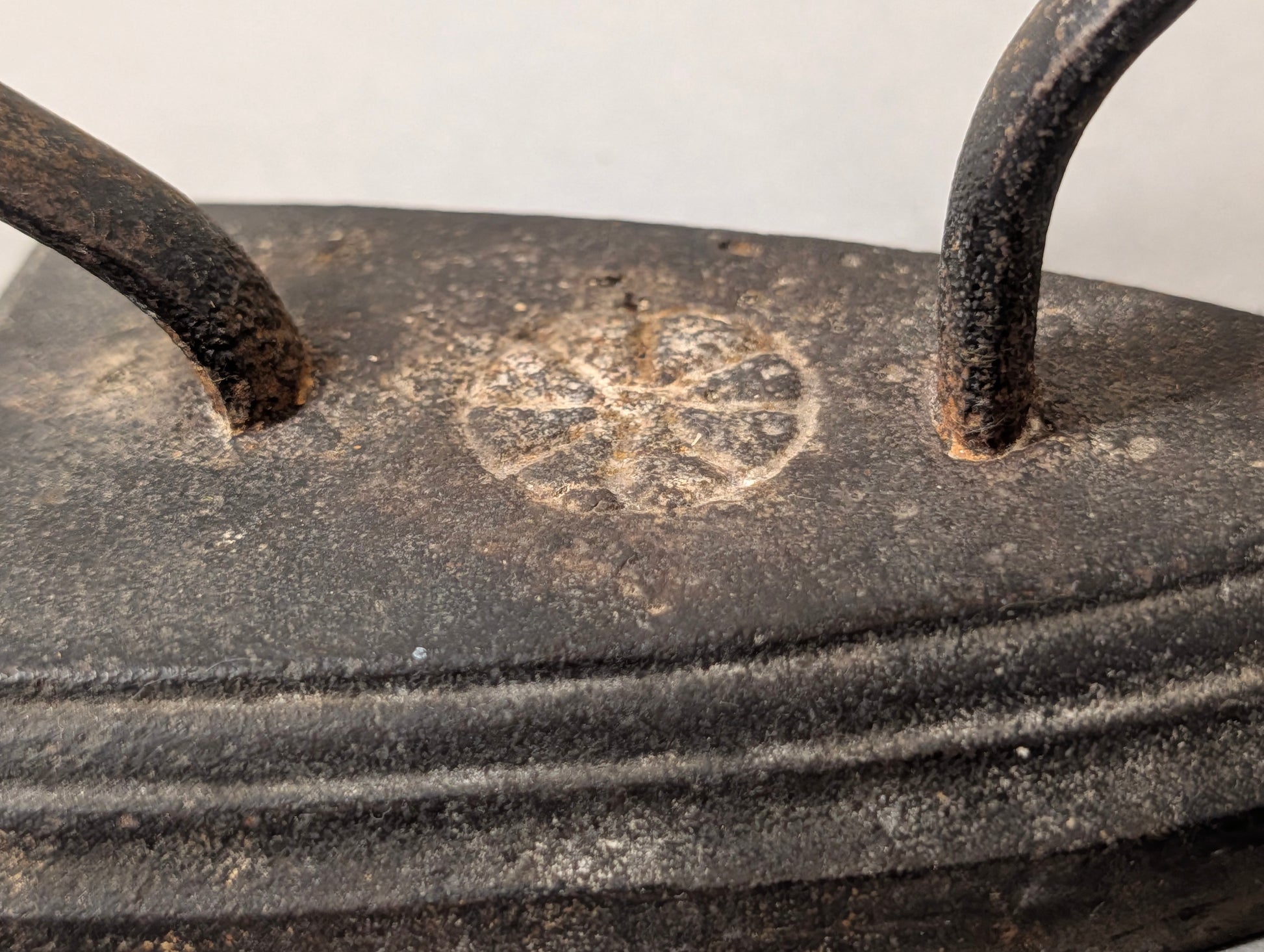 Detailaufnahme der Rosetten-Gussmarke auf dem antiken Bügeleisen, gerippter Zierrand, Gusseisen mit Patina