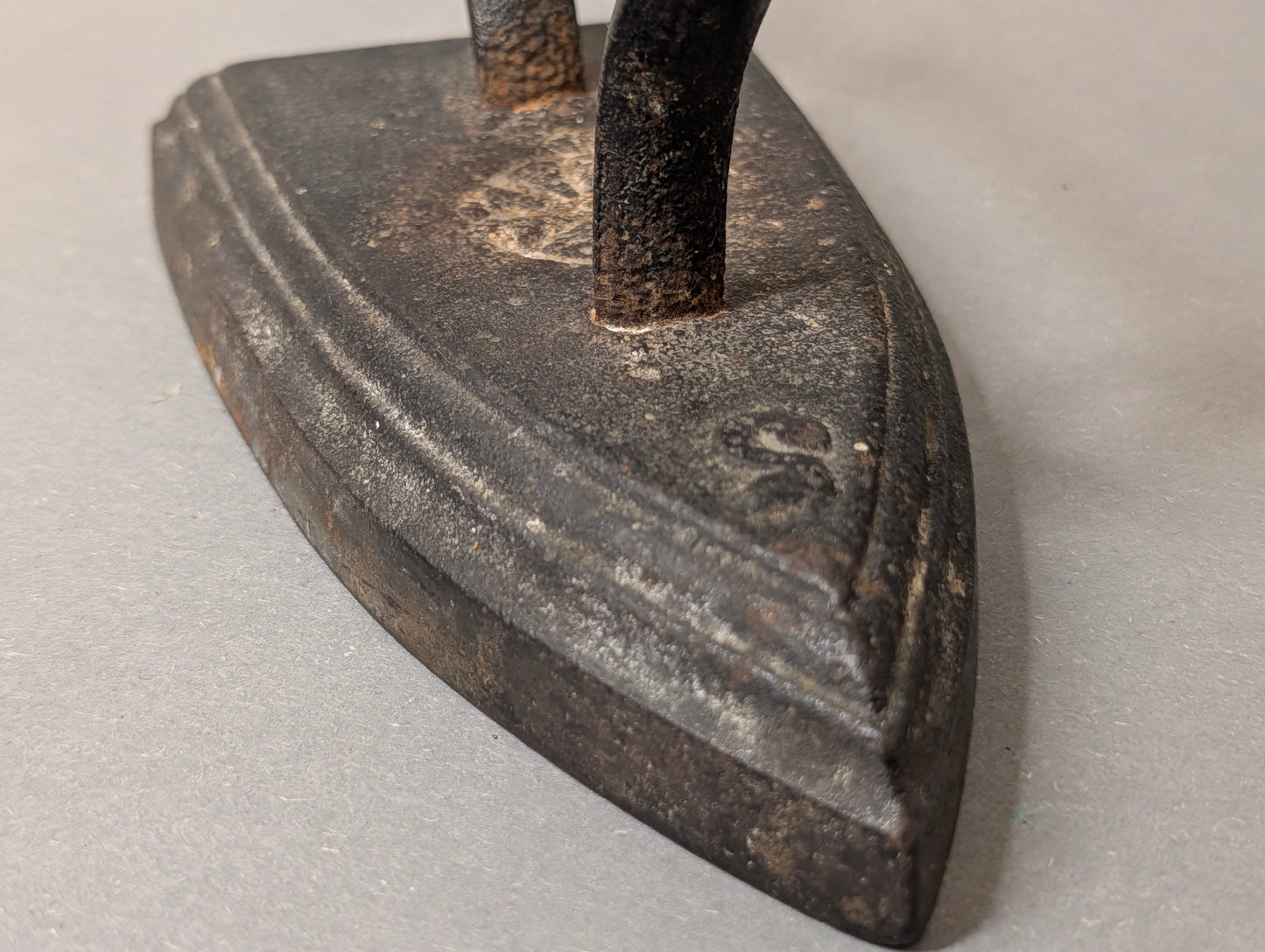Nahaufnahme der Spitze des Gusseisen-Bügeleisens mit umlaufendem Zierrand und Gussmarke, antikes Plätteisen