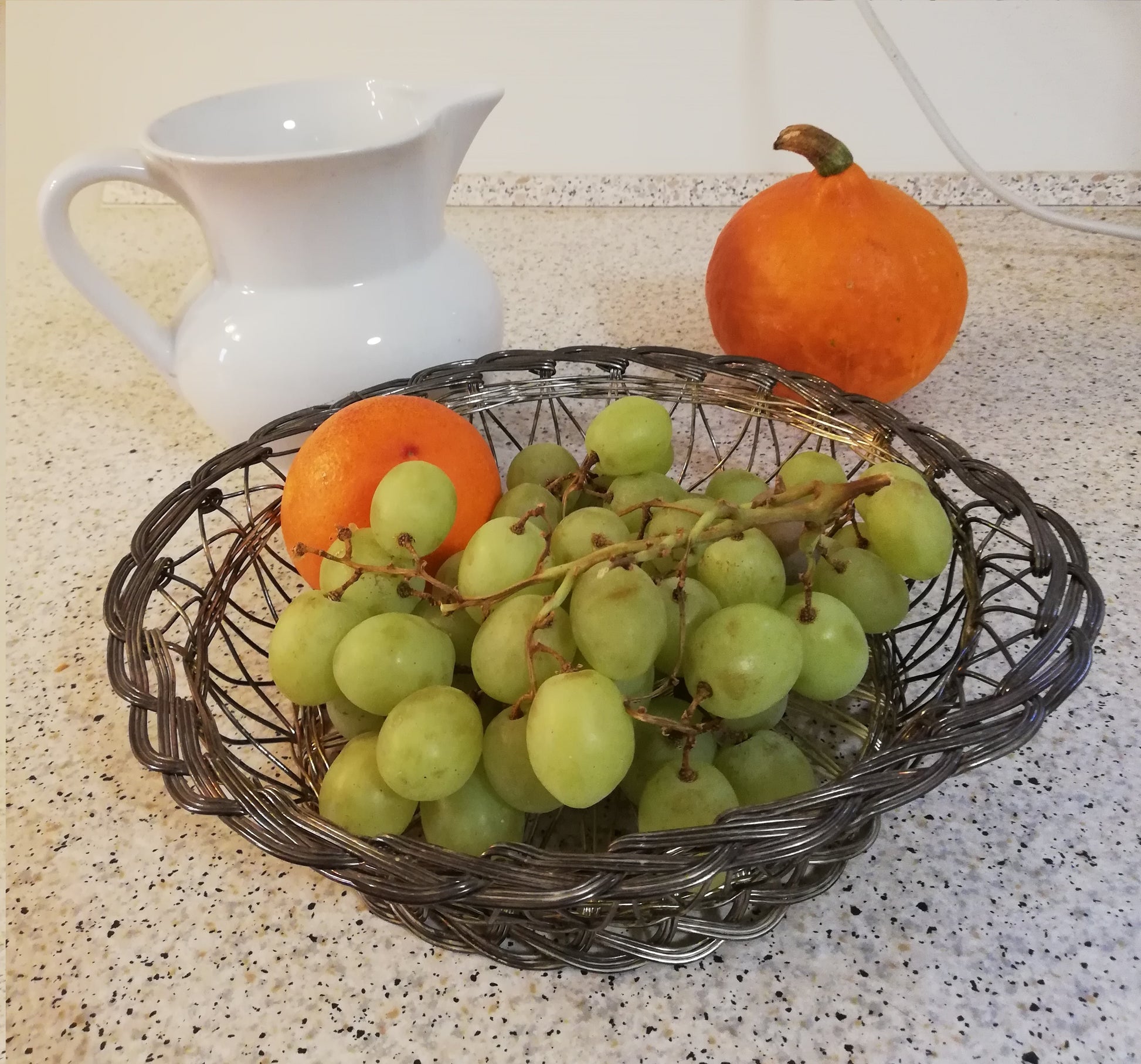 Vintage Drahtschale gefüllt mit Weintrauben und Orange auf einer Küchenarbeitsplatte