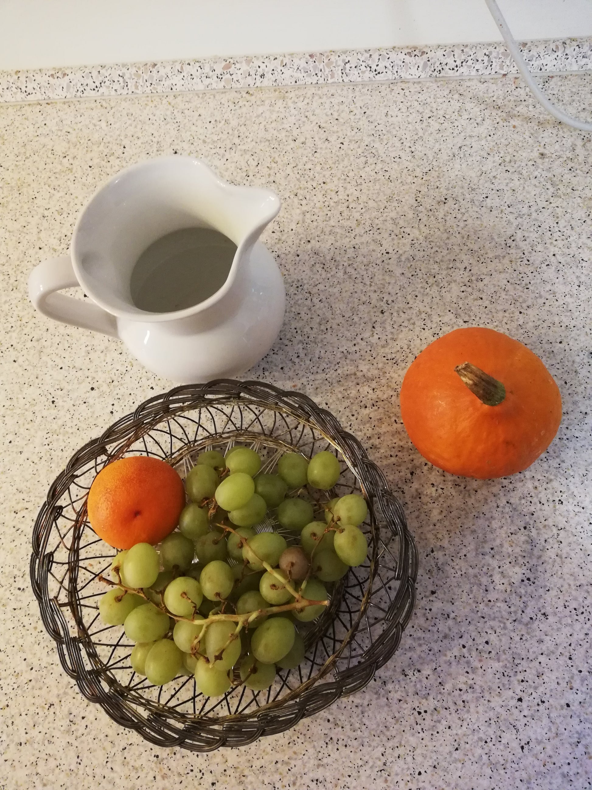 Obstschale aus Draht von oben, gefüllt mit grünen Trauben und zwei Orangen