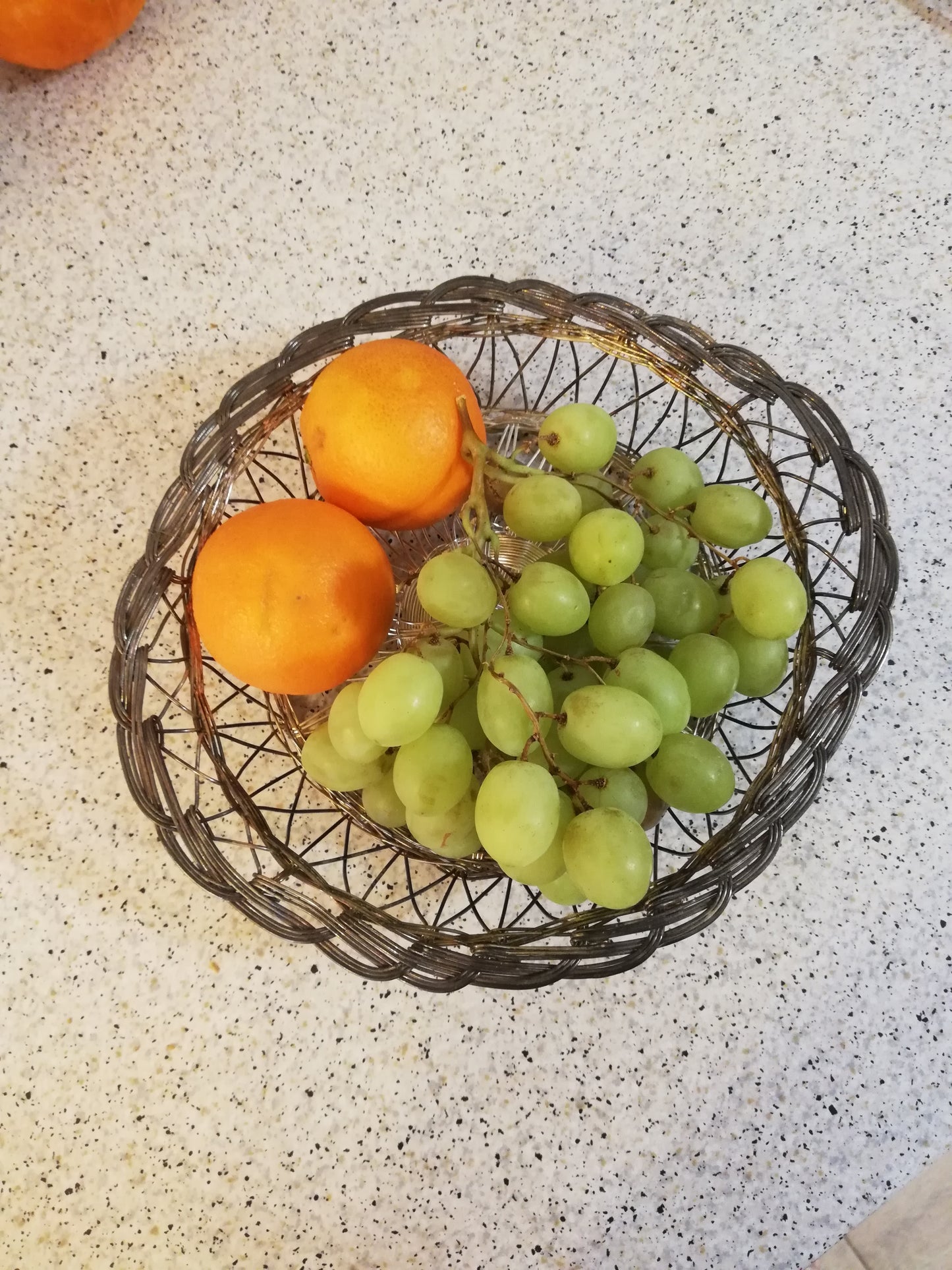 Obstschale aus Draht von oben, gefüllt mit grünen Trauben und zwei Orangen