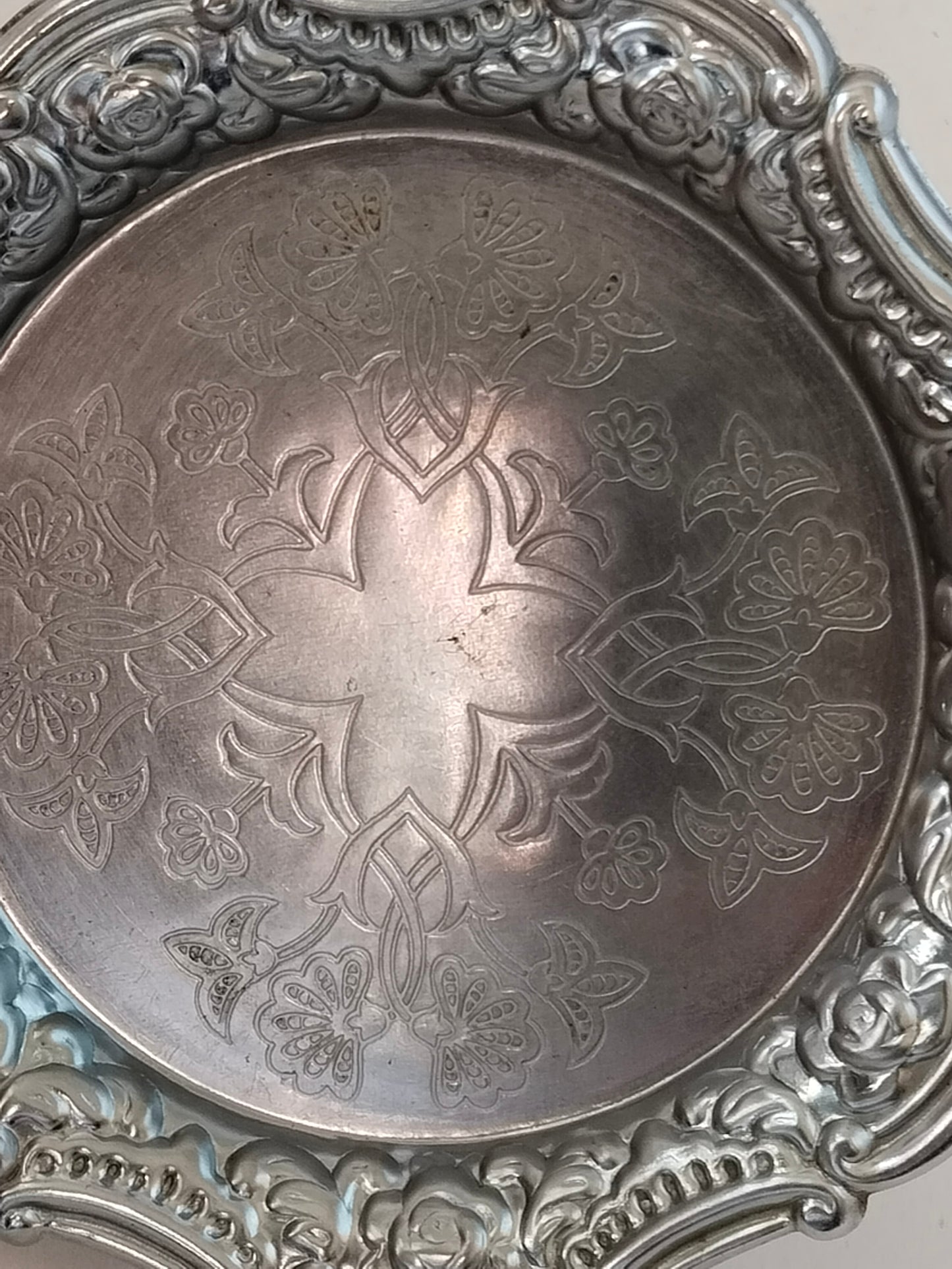 Nahaufnahme der floralen Gravur im Zentrum eines versilberten Untersetzers.