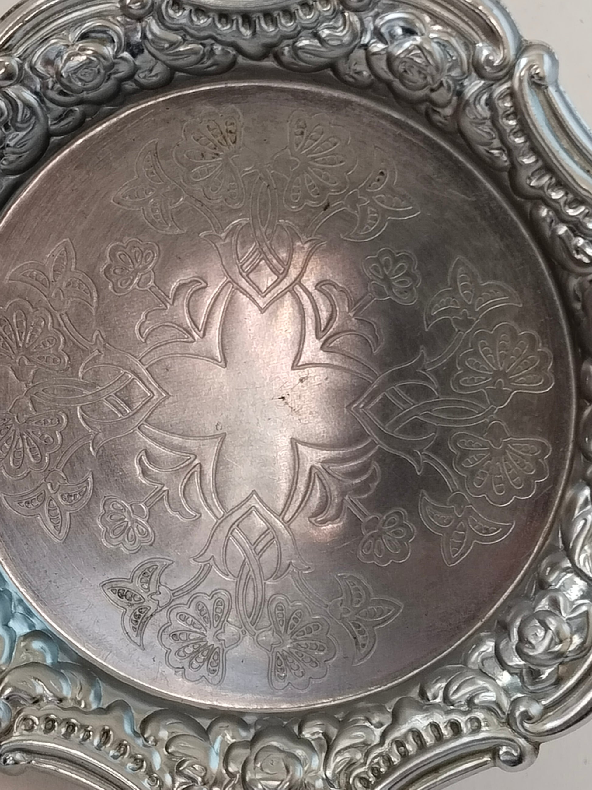 Nahaufnahme der floralen Gravur im Zentrum eines versilberten Untersetzers.