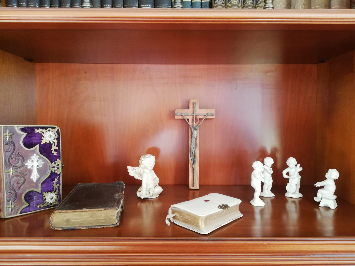 Handgeschnitztes Holzkreuz mit Christus. In einem Bücherregal mit Engeln.