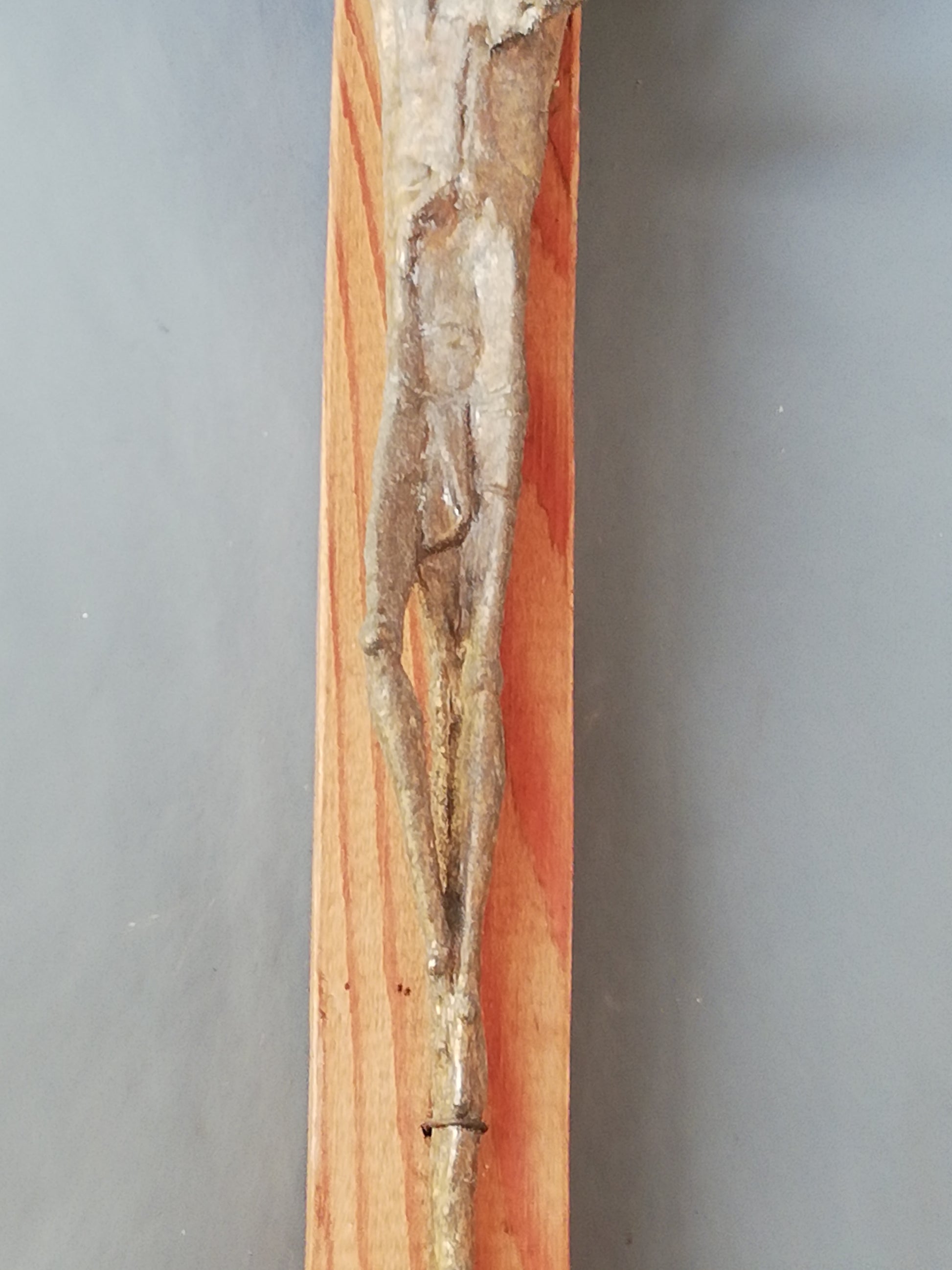 Handgeschnitztes Holzkreuz mit Christus. Unterer Teil des Kreuzes in Nahaufnahme.
