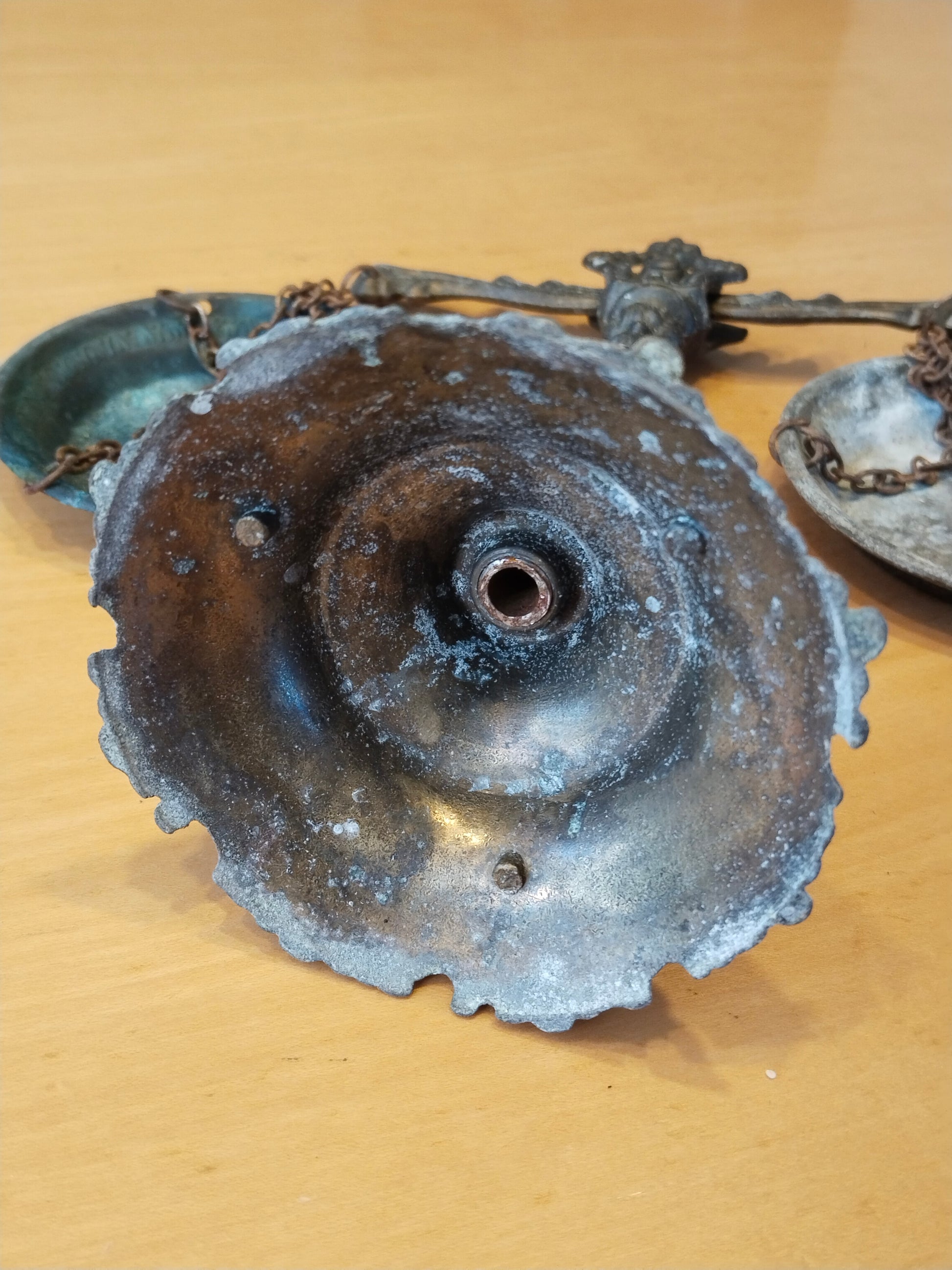 Antike Balkenwaage aus Gussmetall mit zwei Schalen an Eisenketten, Ansicht von unten auf das Innere des Sockels.
