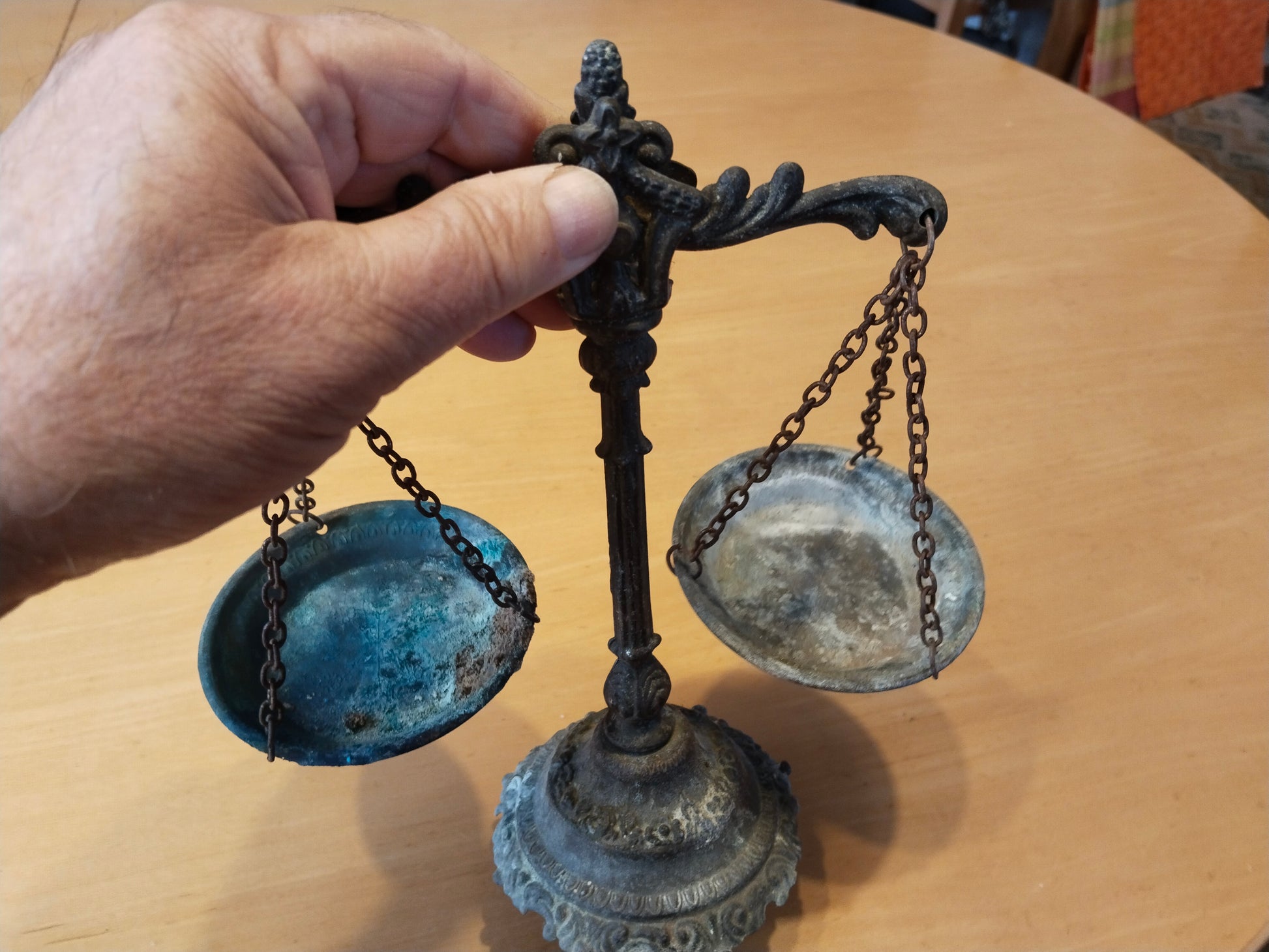 Antike Balkenwaage aus Gussmetall mit zwei Schalen an Eisenketten, Gesamtansicht frontal. In einer Hand zum Größenvergleich.
