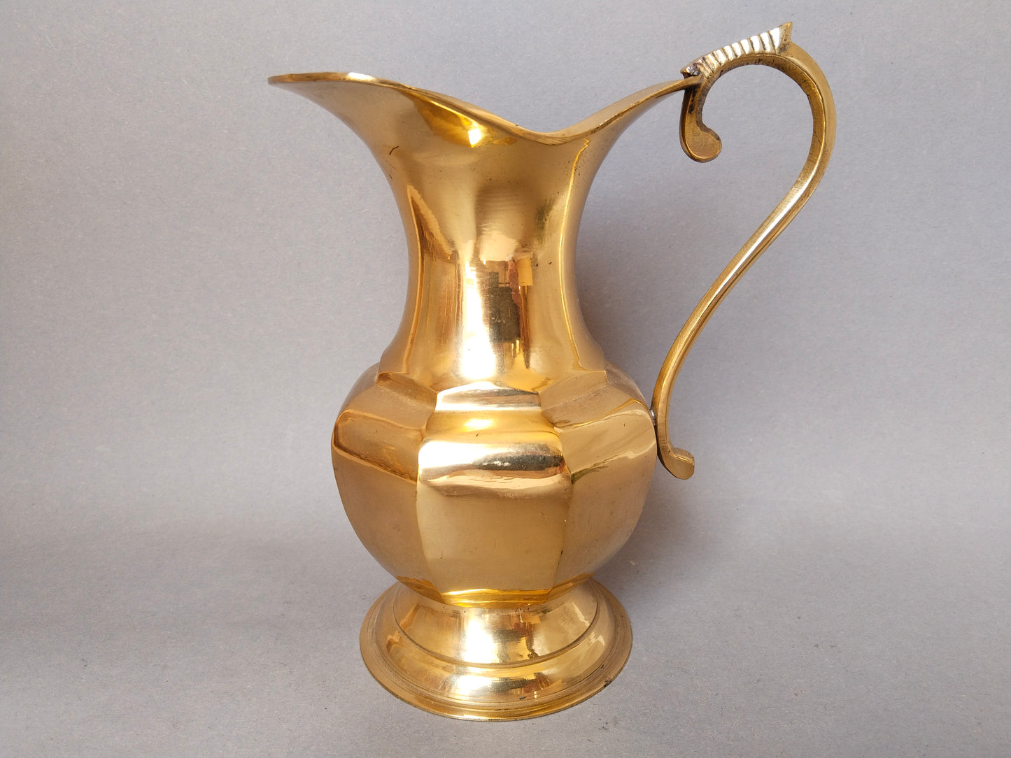 Klassischer Vintage-Messingkrug mit facettiertem Bauch und elegantem Henkel vor grauem Hintergrund