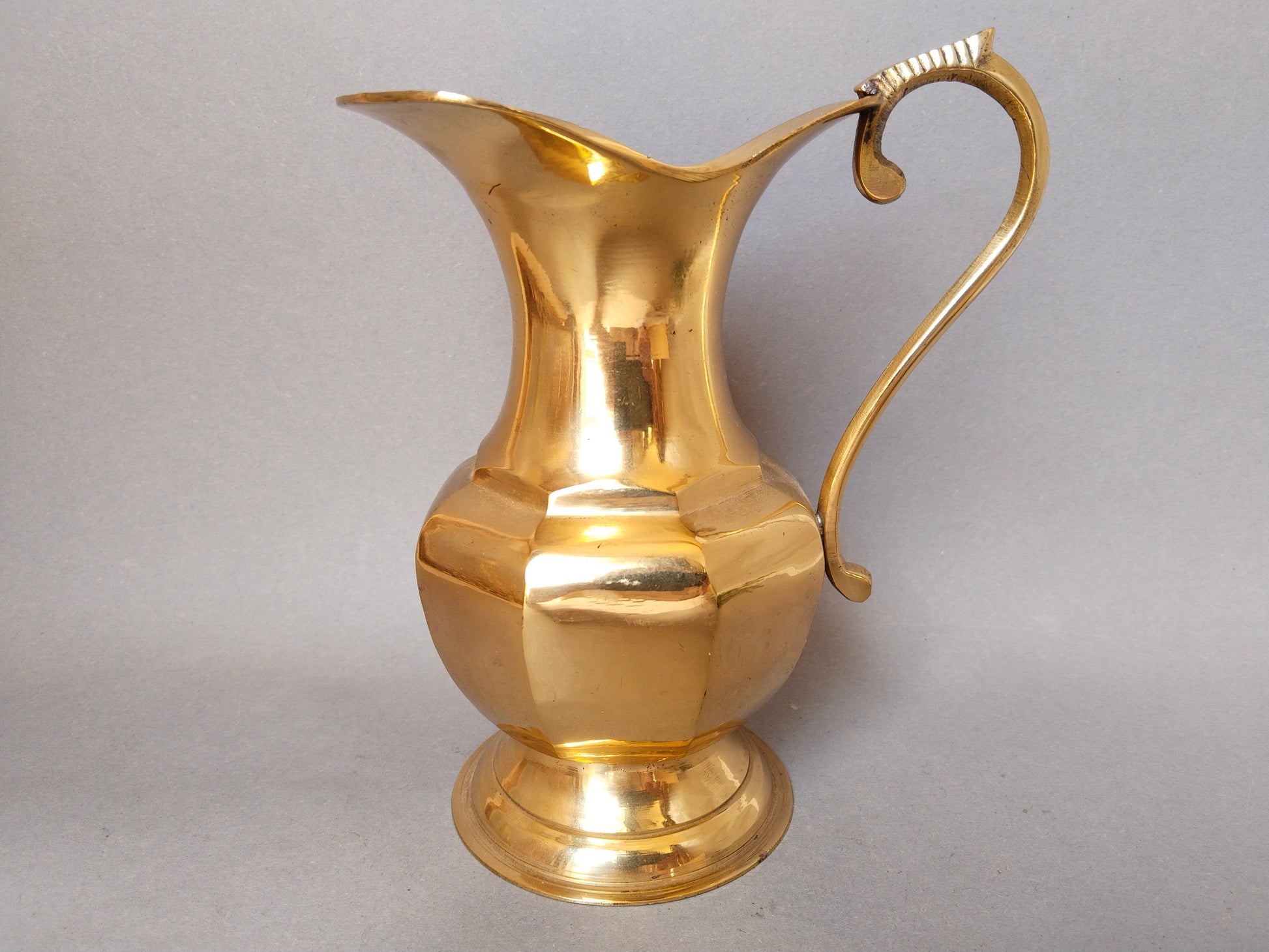 Klassischer Vintage-Messingkrug mit facettiertem Bauch und elegantem Henkel vor grauem Hintergrund