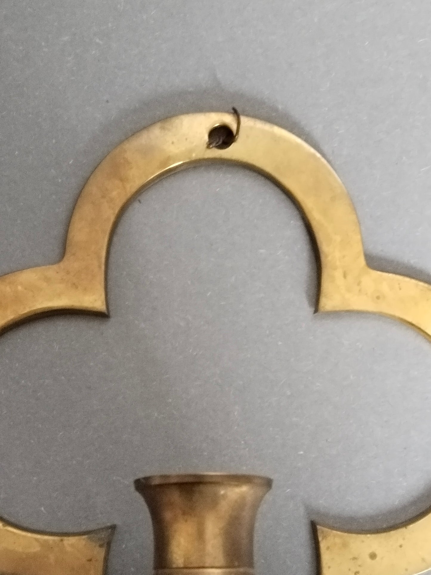 Detailaufnahme der oberen Rundung des Vierpass-Messinghalters mit Aufhängeloch.
