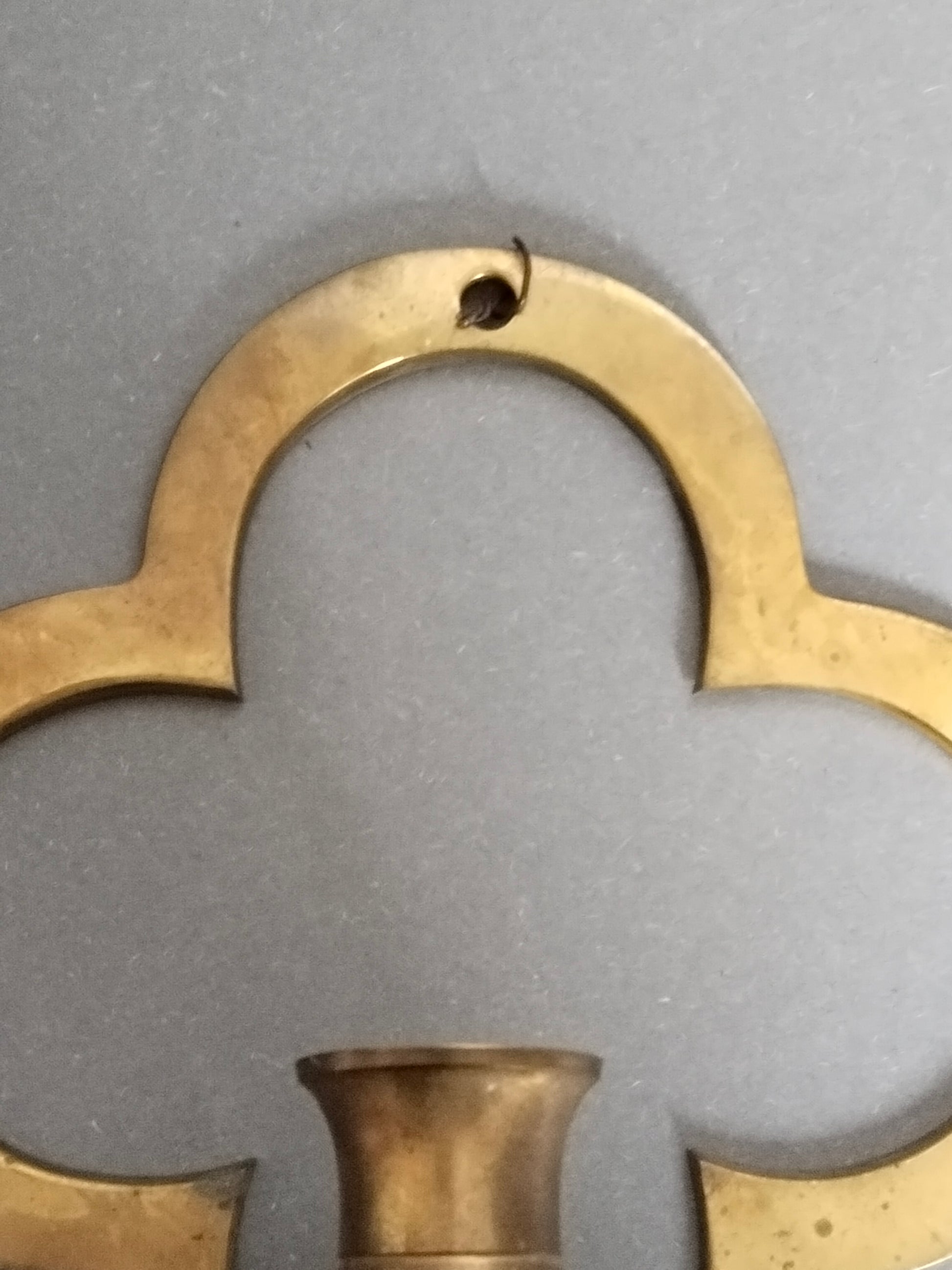 Detailaufnahme der oberen Rundung des Vierpass-Messinghalters mit Aufhängeloch.