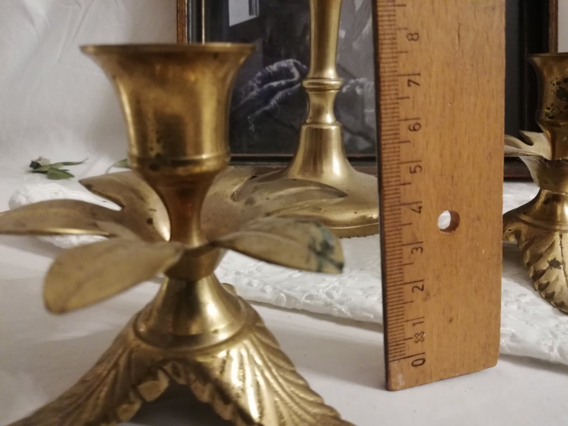 Zwei antike Messing-Kerzenständer mit Akanthusblatt-Fuß auf weißer Spitzendecke. Zusammen mit einem Lineal.