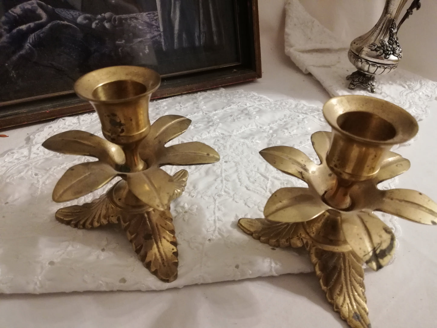 Zwei antike Messing-Kerzenständer mit Akanthusblatt-Fuß auf weißer Spitzendecke