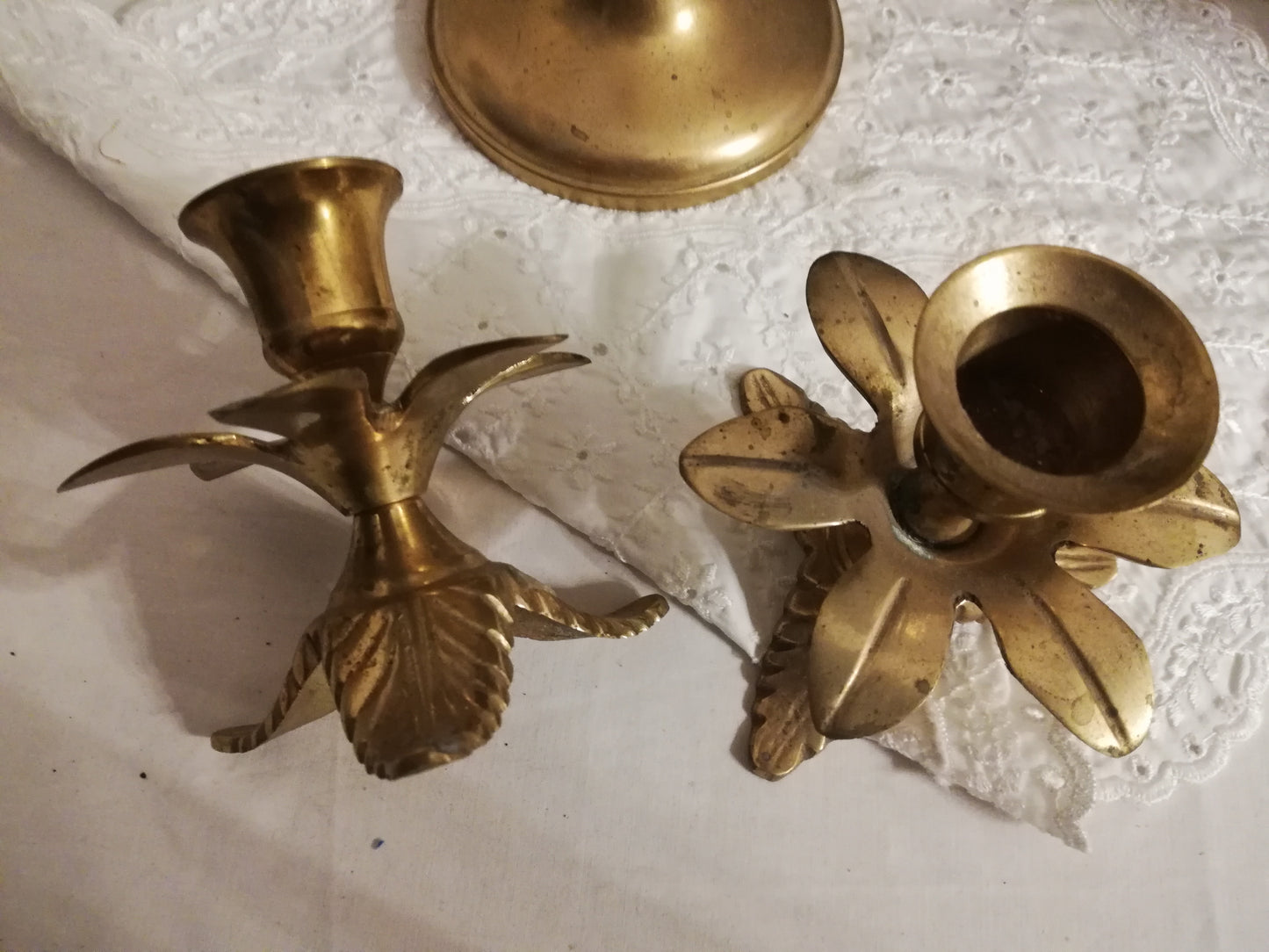 Zwei antike Messing-Kerzenständer mit Akanthusblatt-Fuß auf weißer Spitzendecke. Ansicht von oben mit einem liegenden Kerzenhalter.