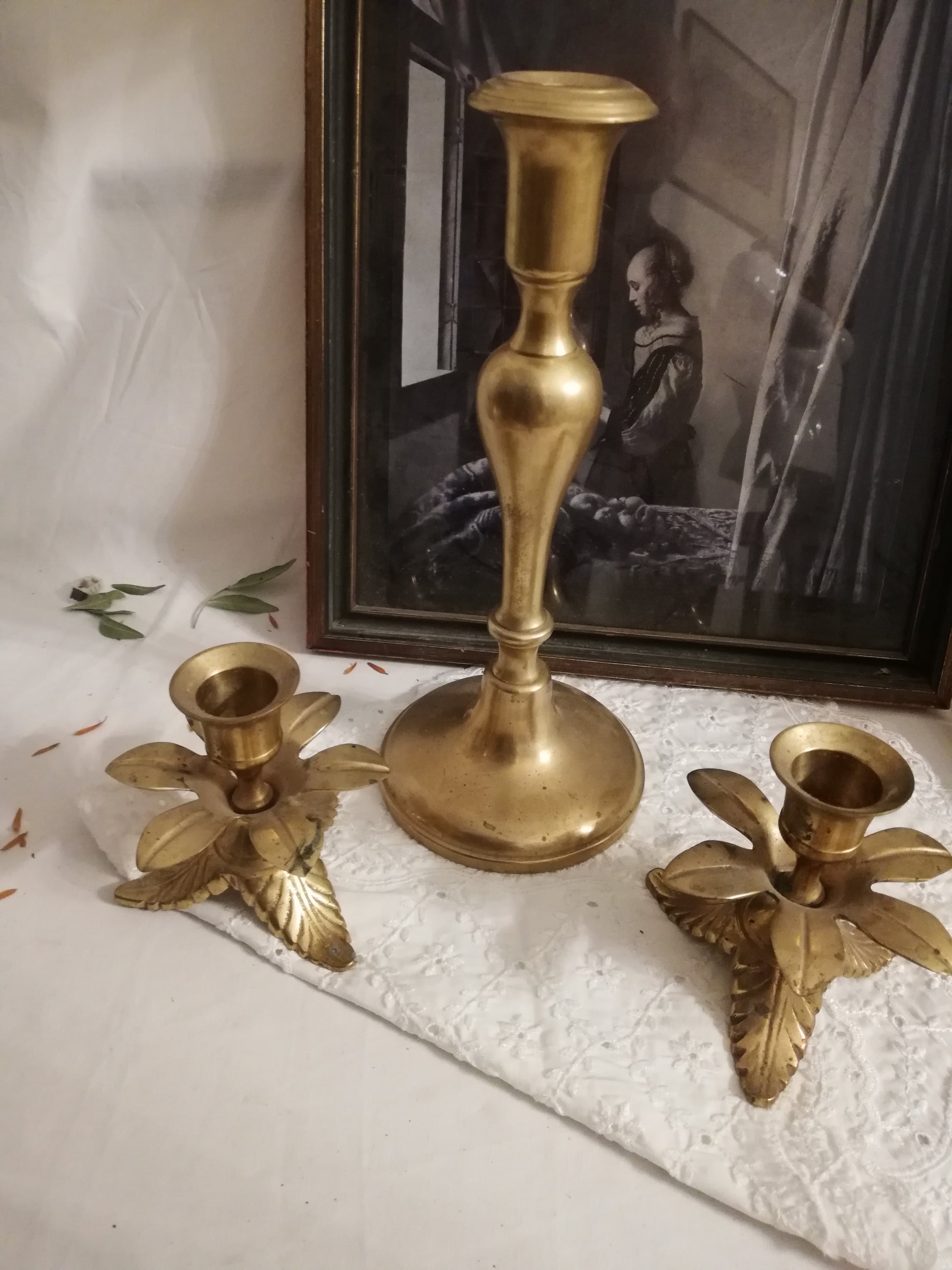 Zwei antike Messing-Kerzenständer mit Akanthusblatt-Fuß auf weißer Spitzendecke. Arrangement mit großem Kerzenständer.