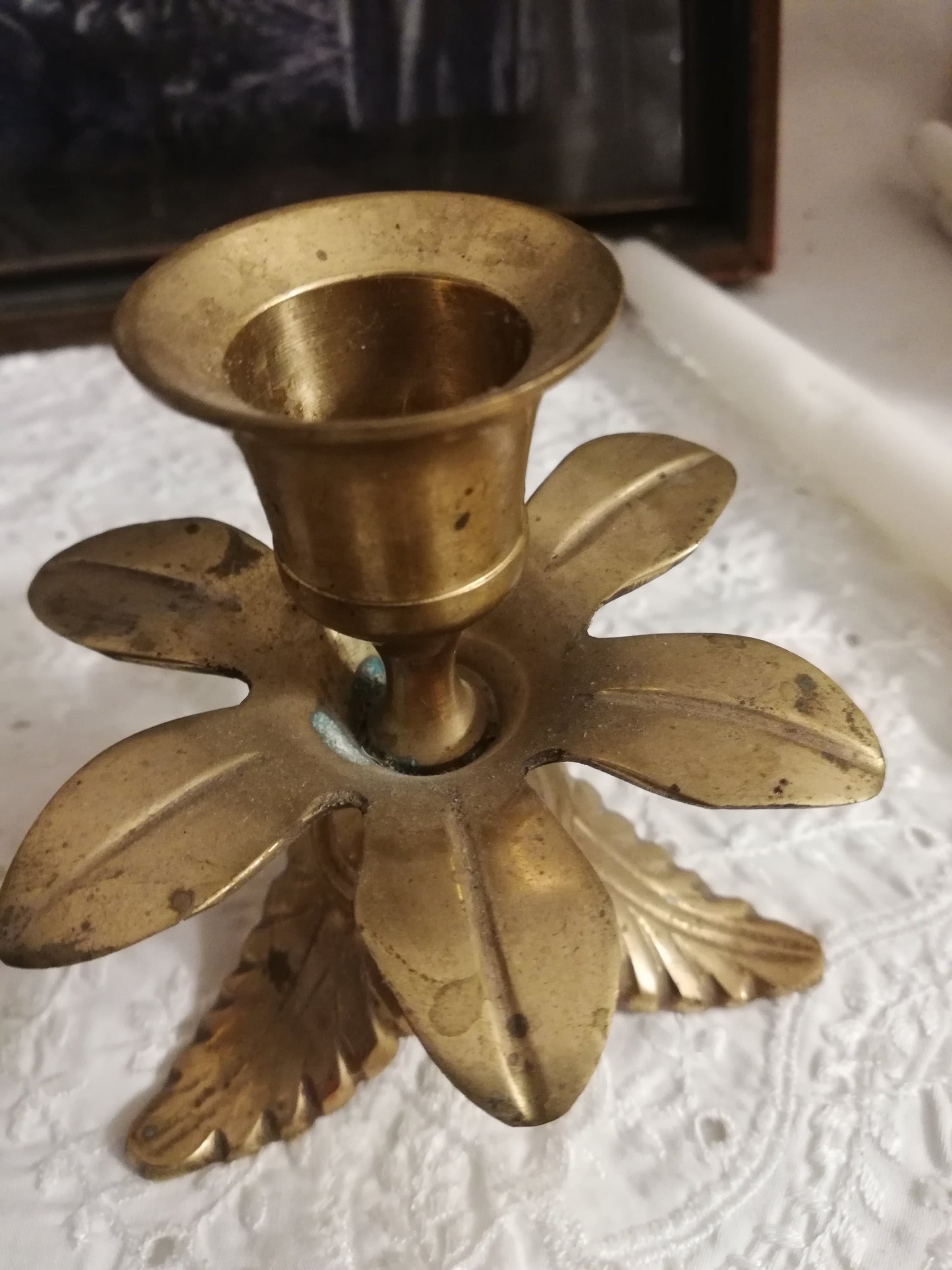 Zwei antike Messing-Kerzenständer mit Akanthusblatt-Fuß auf weißer Spitzendecke. Nahaufnahme von einem einzelnen Kerzenhalter.