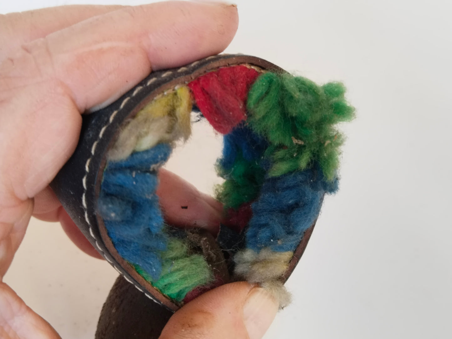 Geöffnete Lederschlaufe mit Blick auf bunte Wollfäden im Inneren
