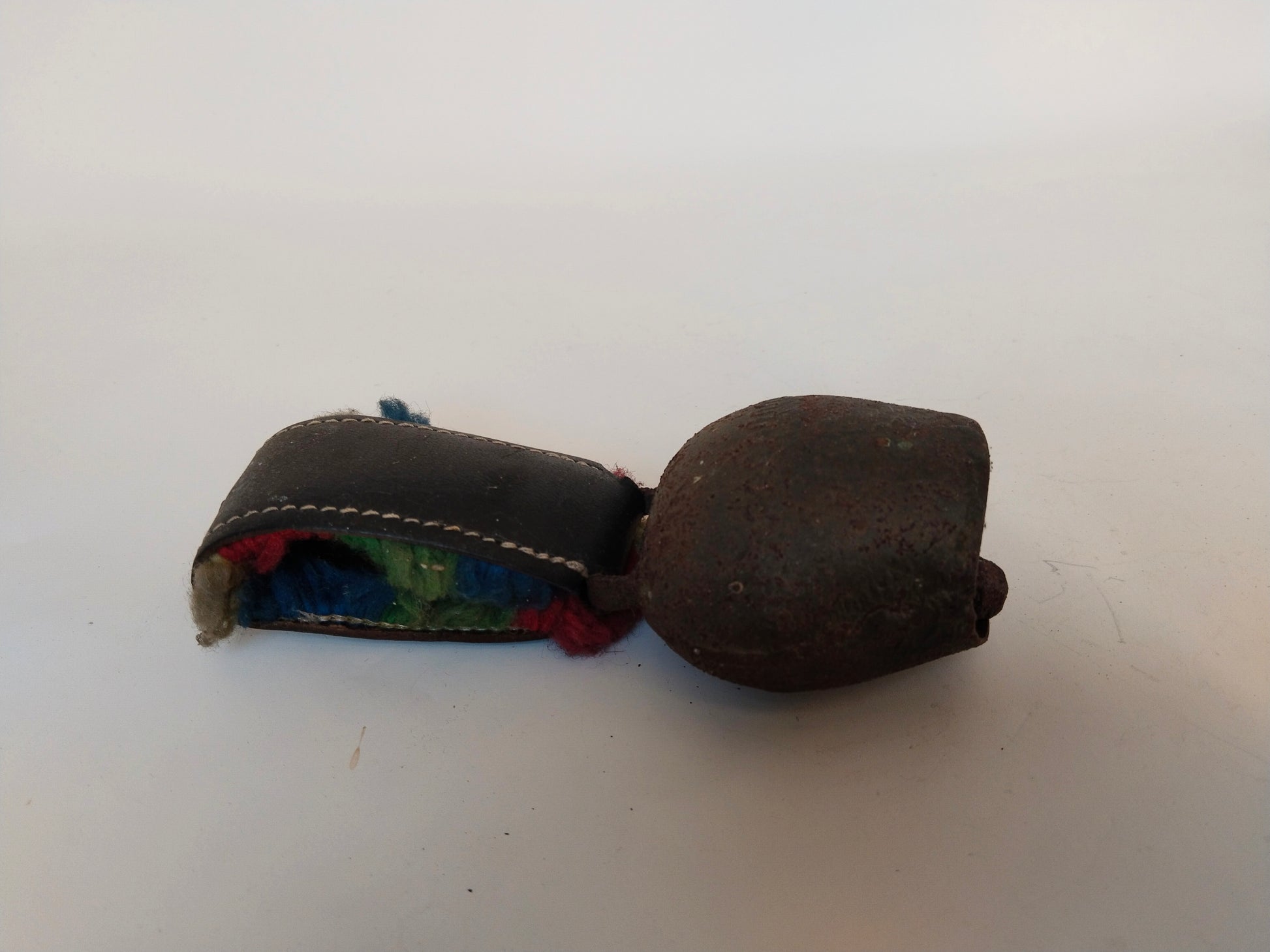 Kuhschelle seitliche Ansicht mit Lederriemen und buntem Wollbesatz
