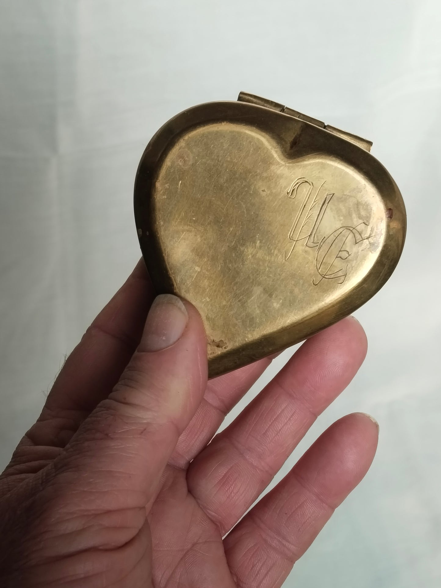 Eine Hand hält die herzförmige Messingdose, um die kompakte Größe von 7x7 cm zu veranschaulichen.