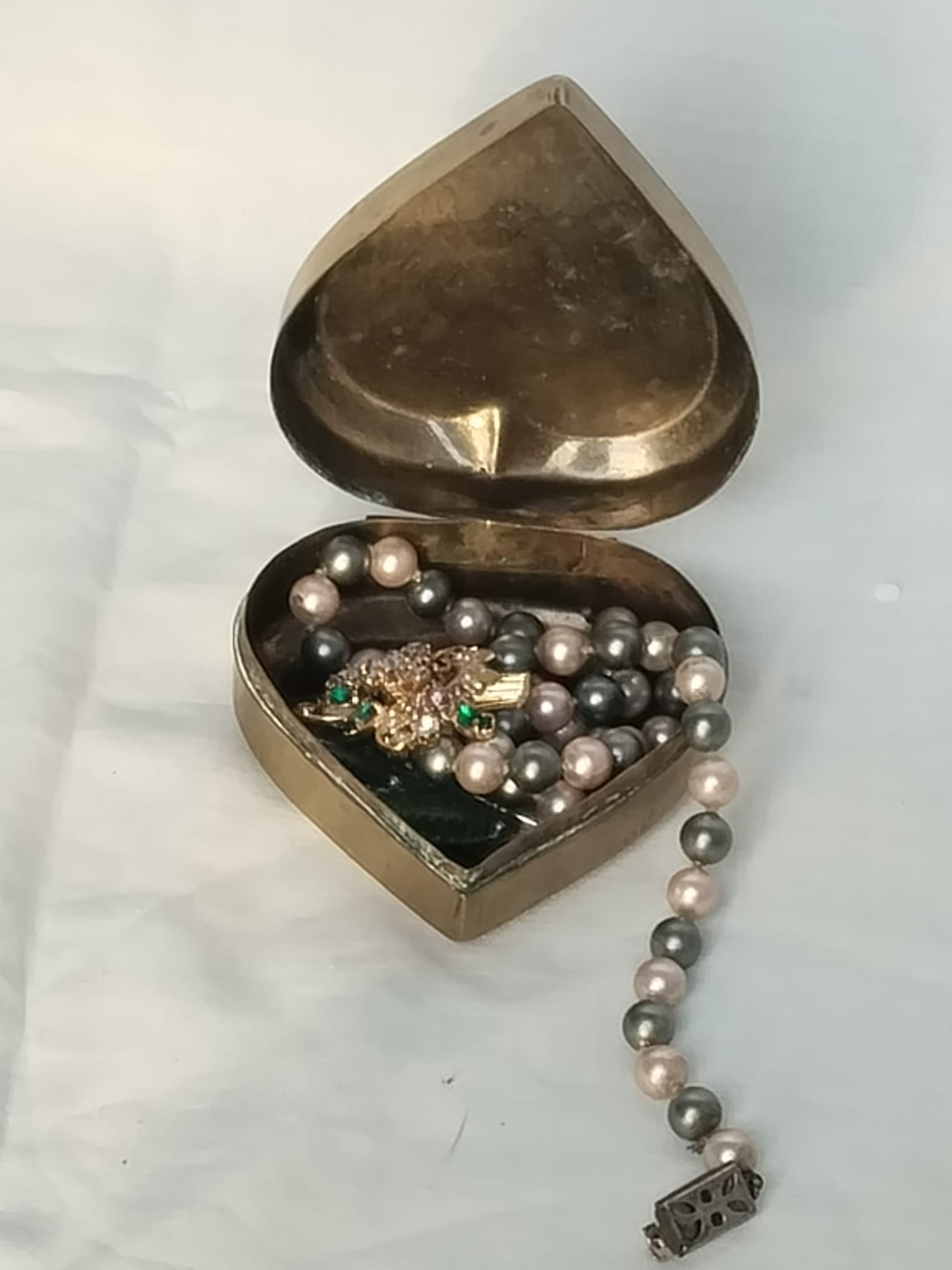 Geöffnete Schatulle gefüllt mit einer Perlenkette und einer Vintage-Brosche als Dekorationsbeispiel.
