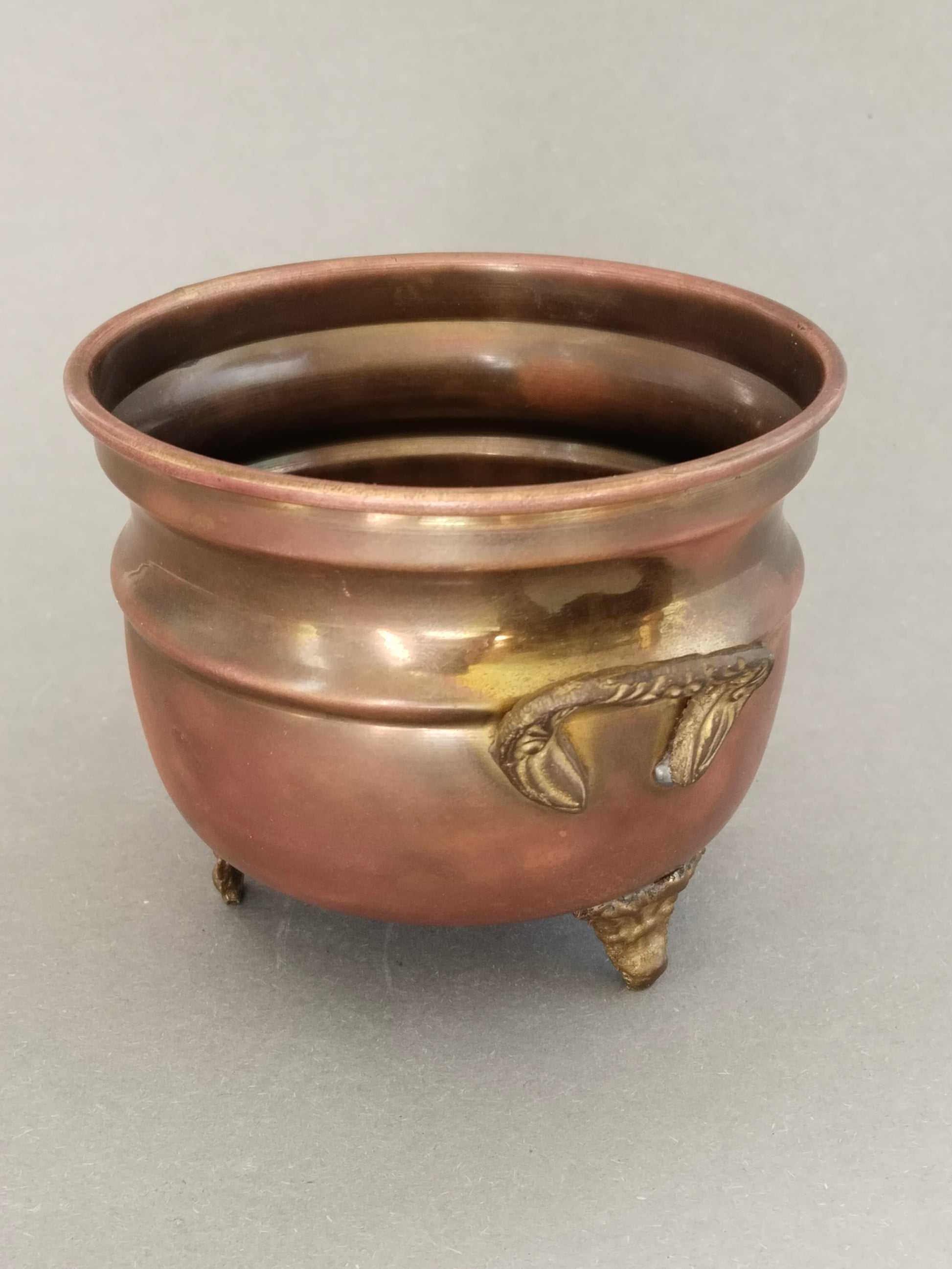 Messingkessel schräg von vorne mit floral verziertem Ringgriff und blattförmigem Zierfuß
