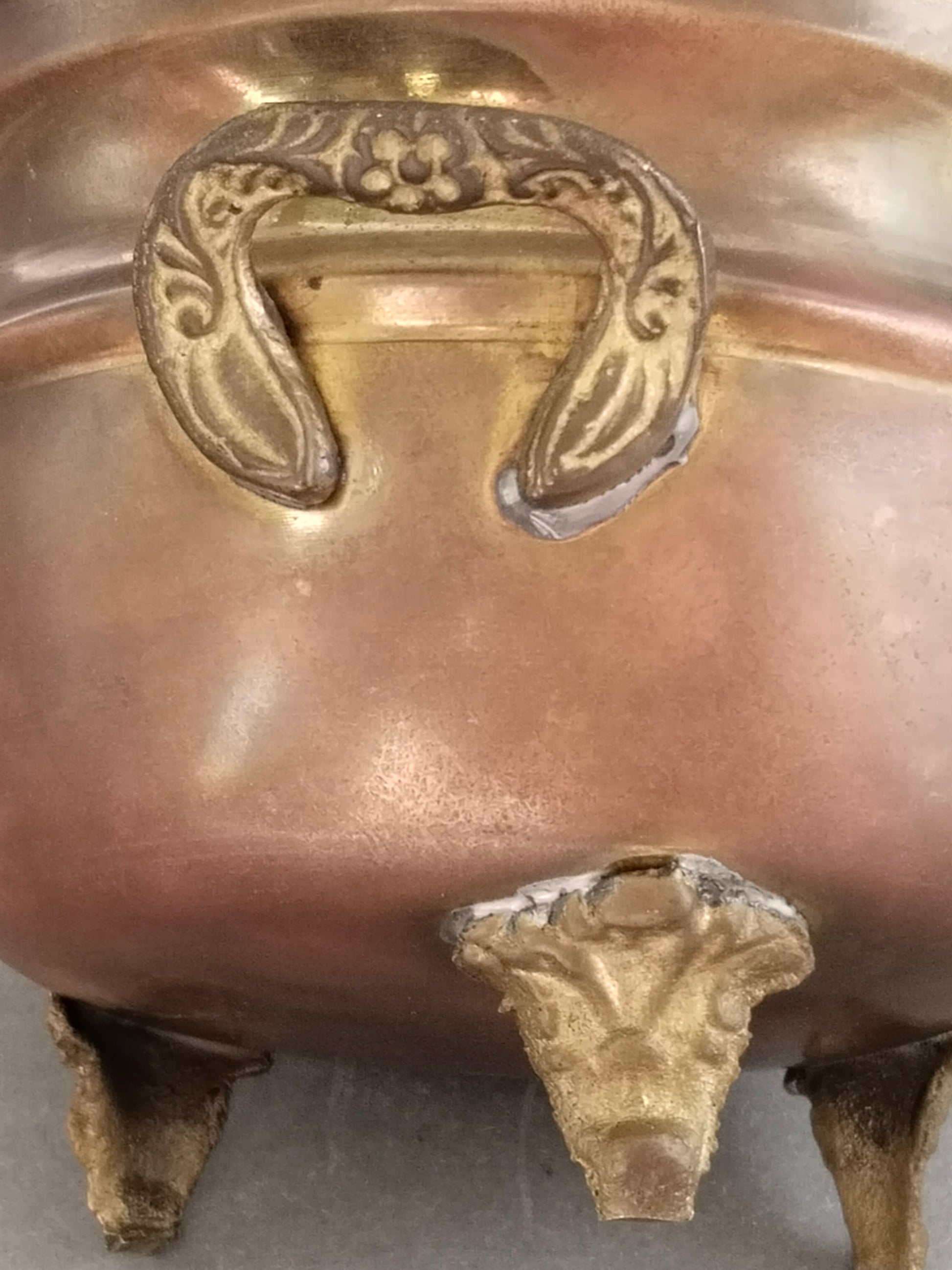 Nahaufnahme des Ringgriffs mit Blüten- und Rankenrelief über dem gelöteten Zierfuß