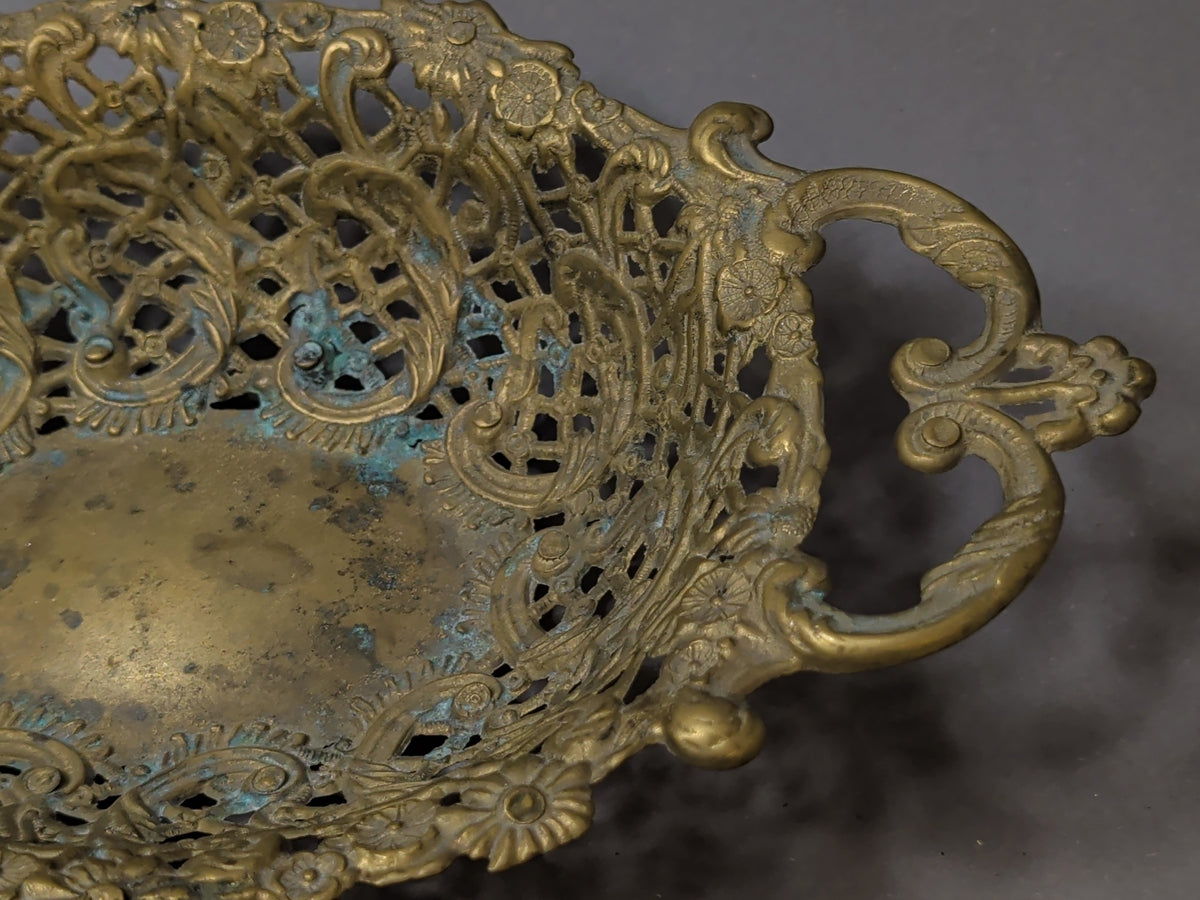 Detail eines S-förmigen Messinggriffs mit Blütenkrone am Ende, daneben Rautengitter und Blütenrosetten mit Grünspan-Patina