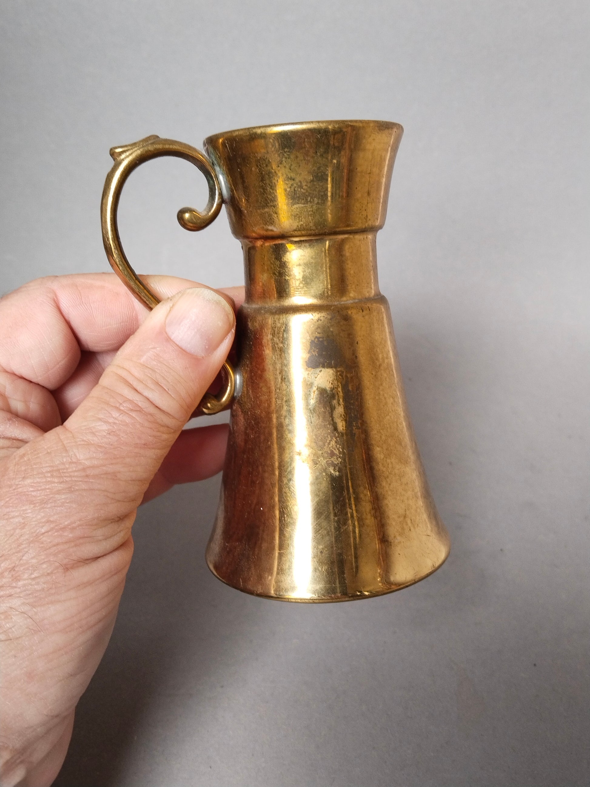 Vintage Messing Krug Vase mit S-Henkel in eine Hand gehalten.