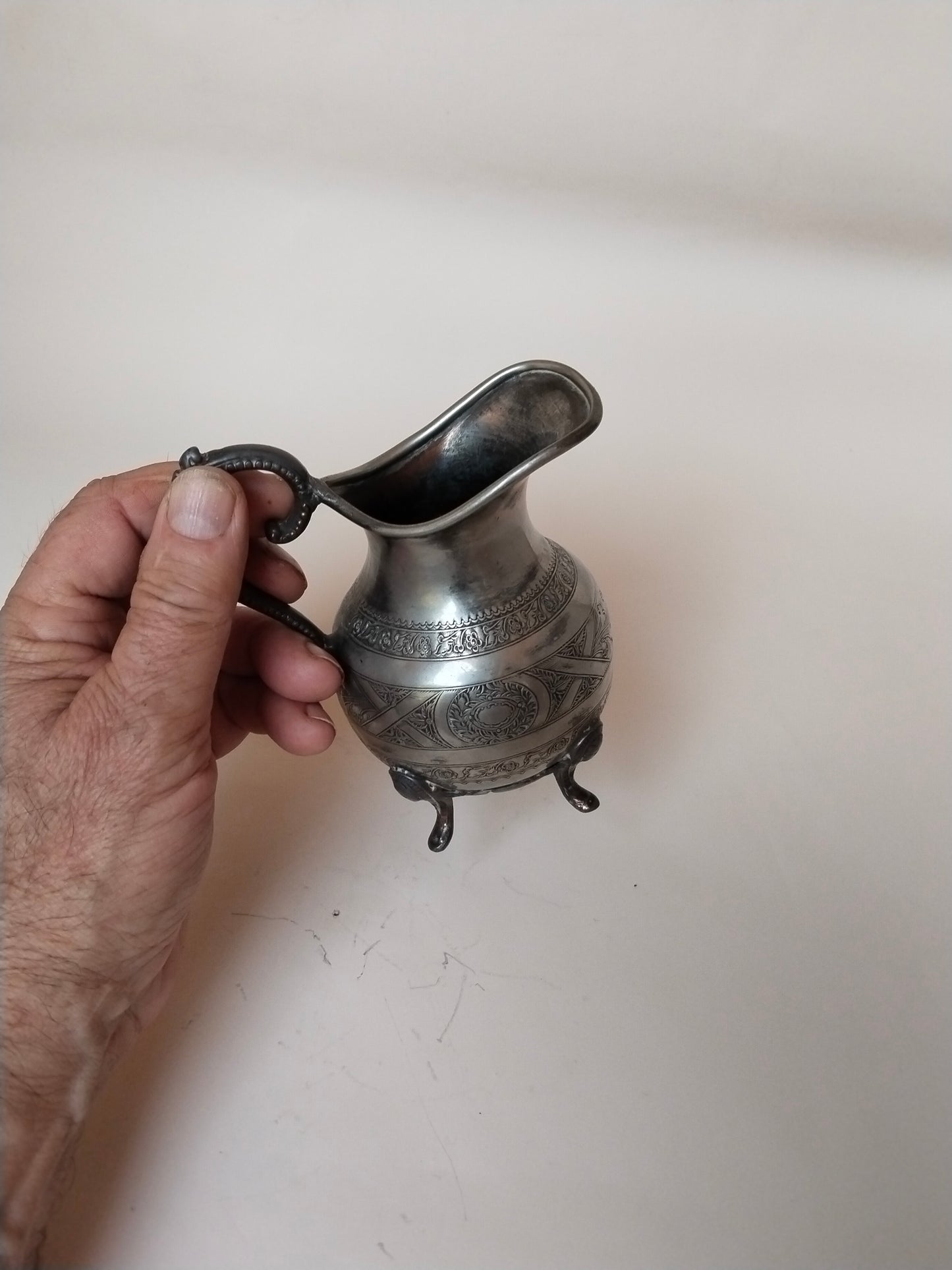 Versilbertes Milchkännchen in der Hand gehalten, Seitenansicht mit Henkel und Schnabel