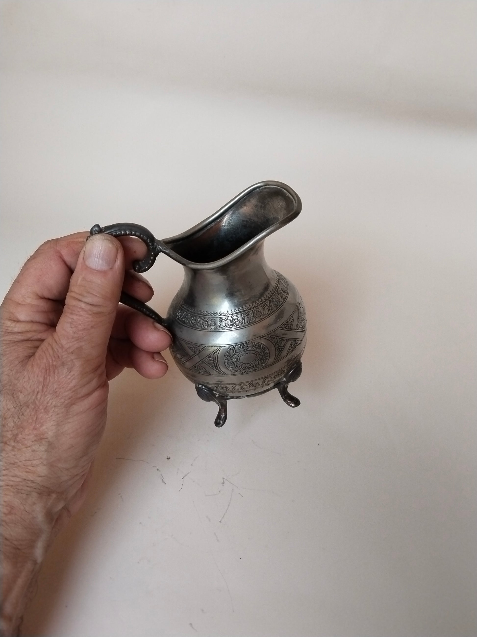 Versilbertes Milchkännchen in der Hand gehalten, Seitenansicht mit Henkel und Schnabel