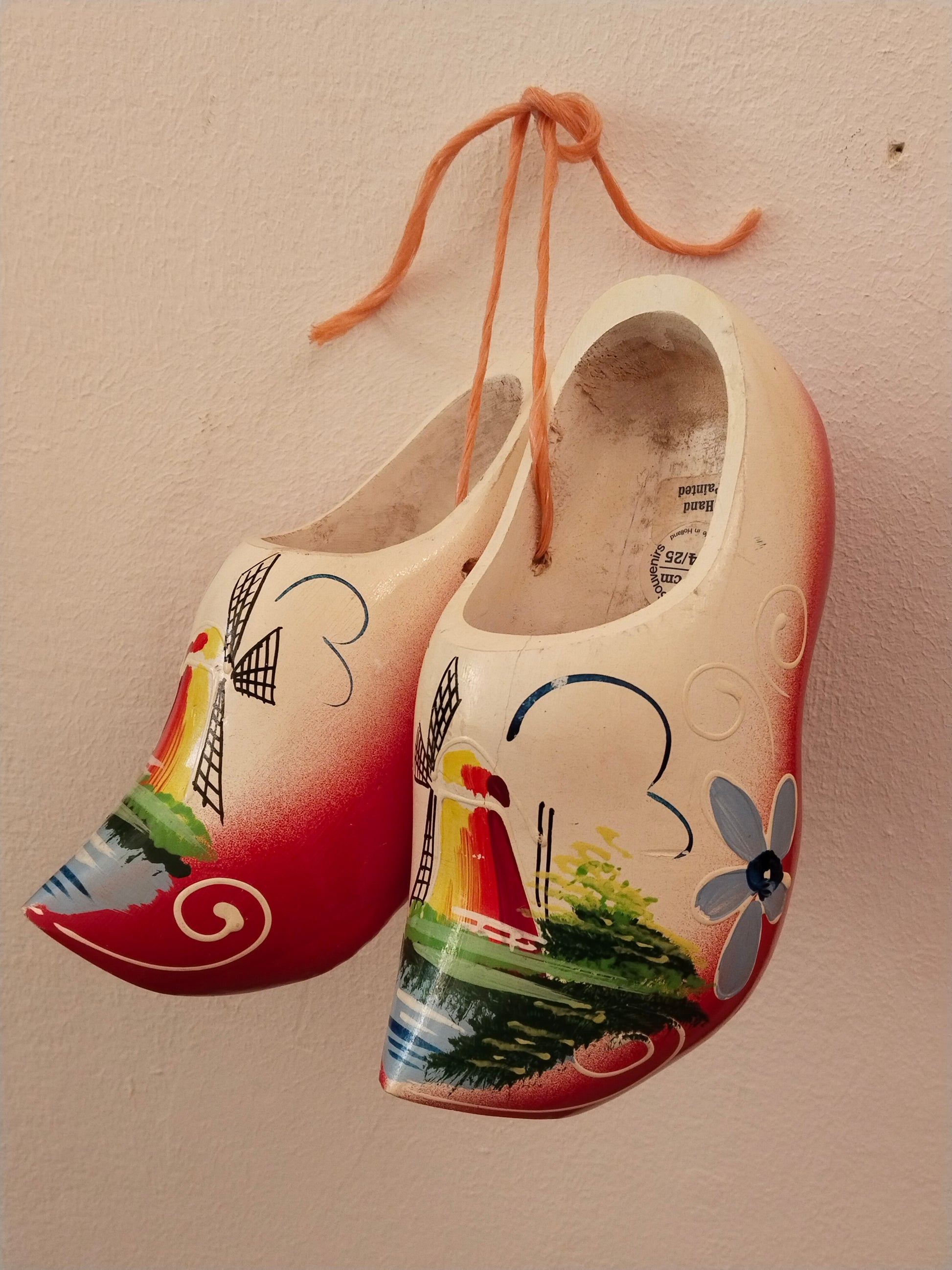 Handbemalte niederländische Holzschuhe Vintage. Beide Schuhe hängen über eine Schnur verbunden an der Wand.