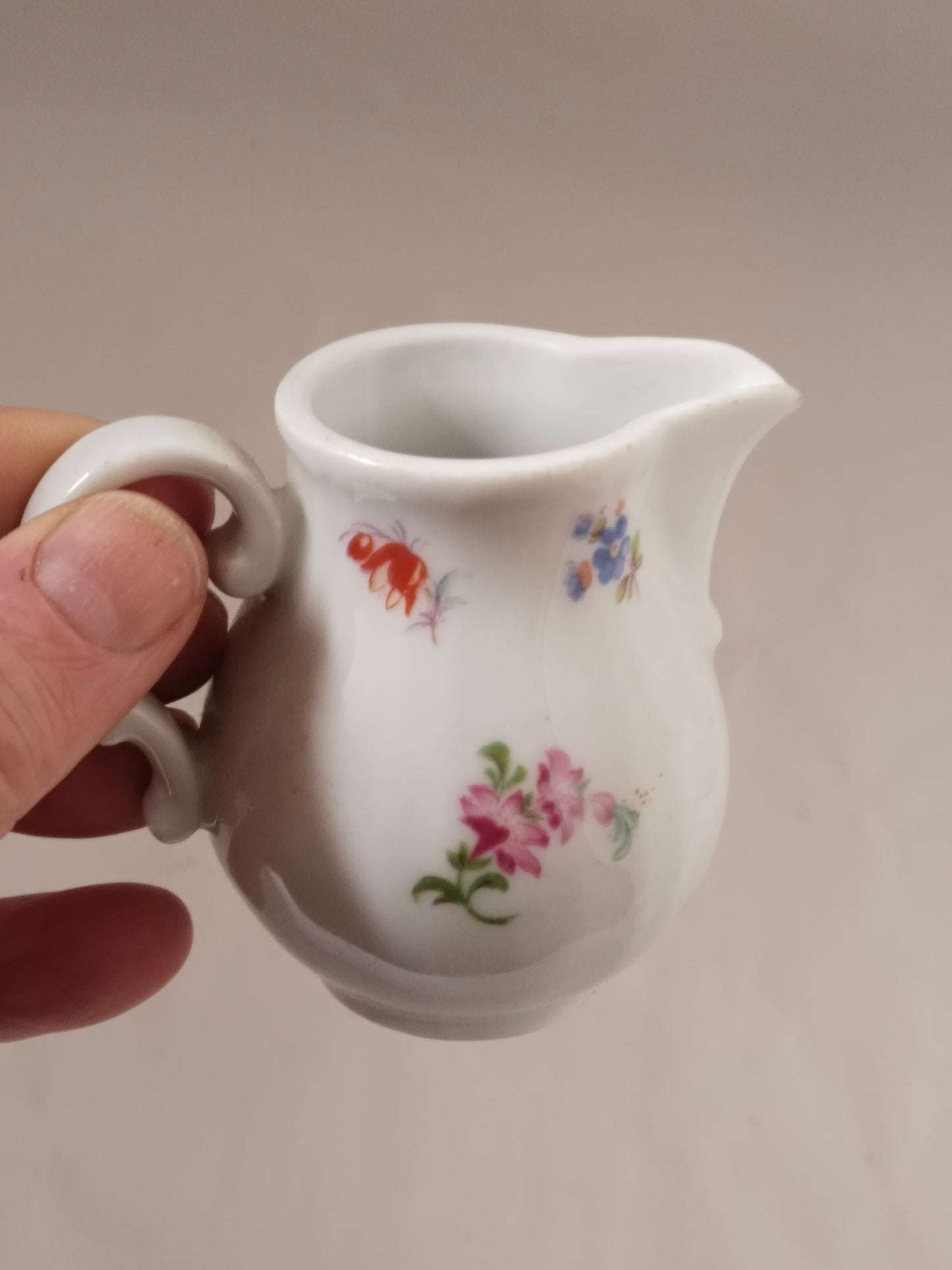 Hand hält ein kleines weißes Milchkännchen, um die kompakte Größe zu verdeutlichen.
