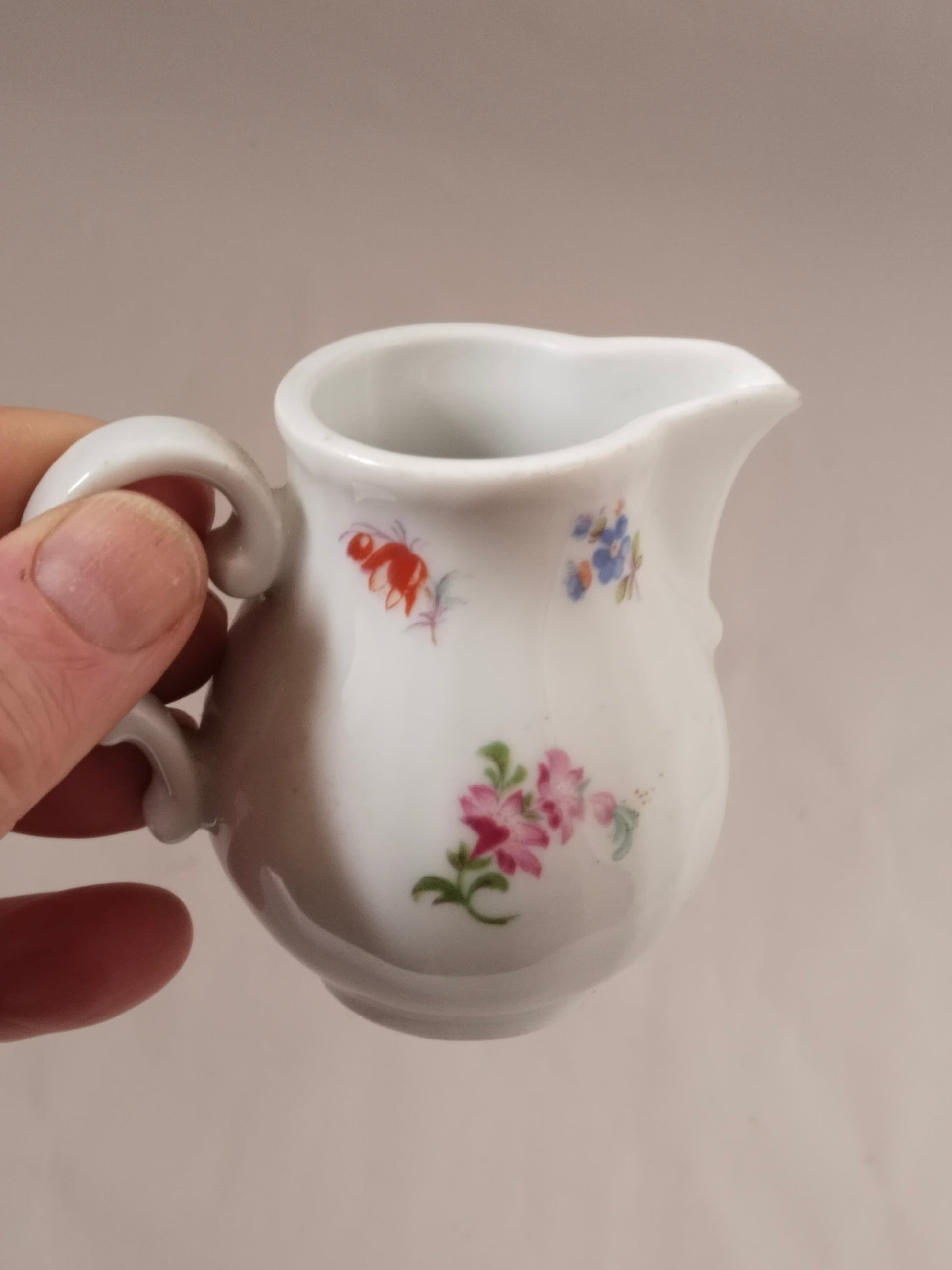 Hand hält ein kleines weißes Milchkännchen, um die kompakte Größe zu verdeutlichen.