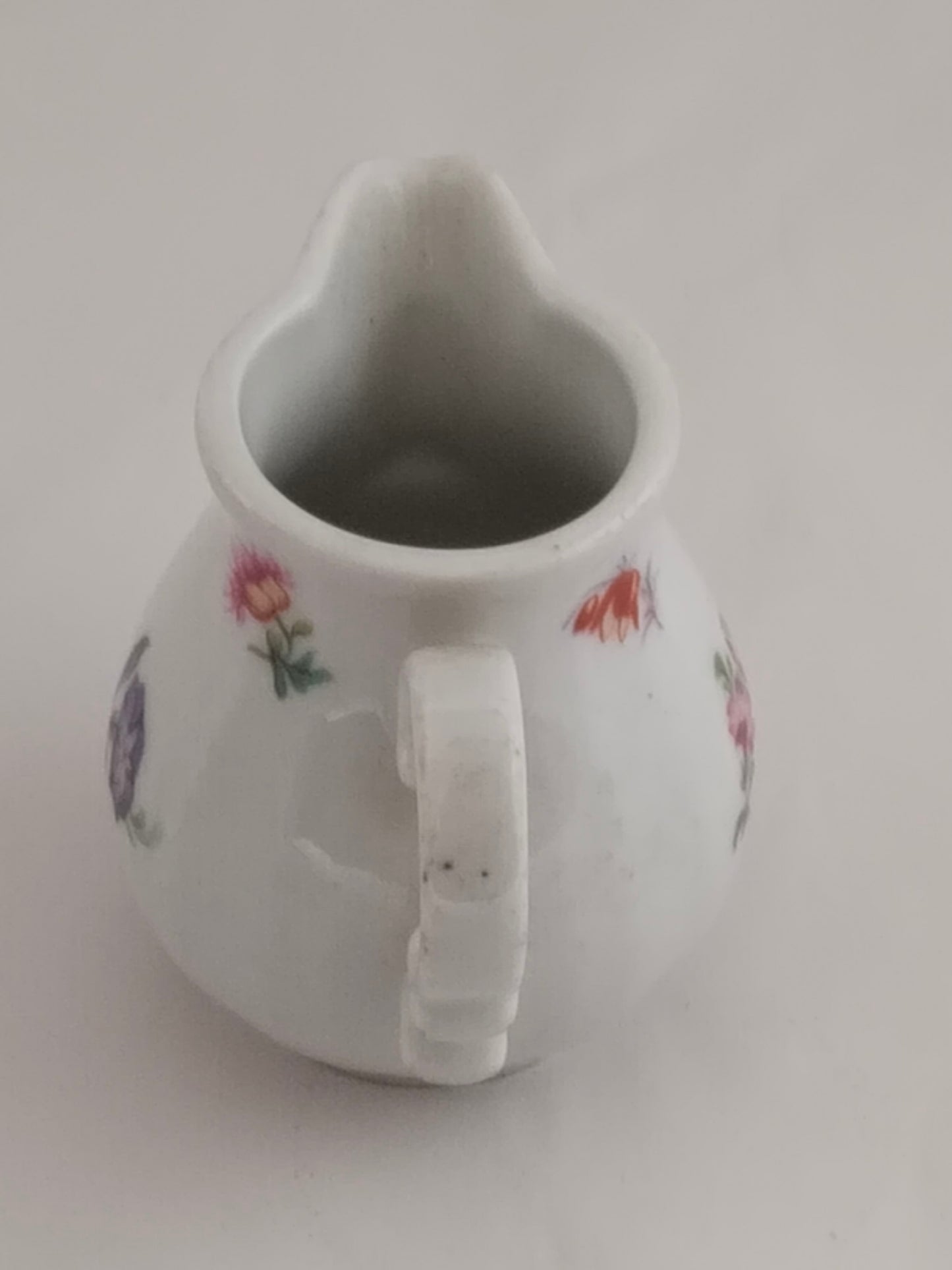 Rückansicht des Milchkännchens mit Fokus auf die glatte weiße Glasur und einzelne Blüten.