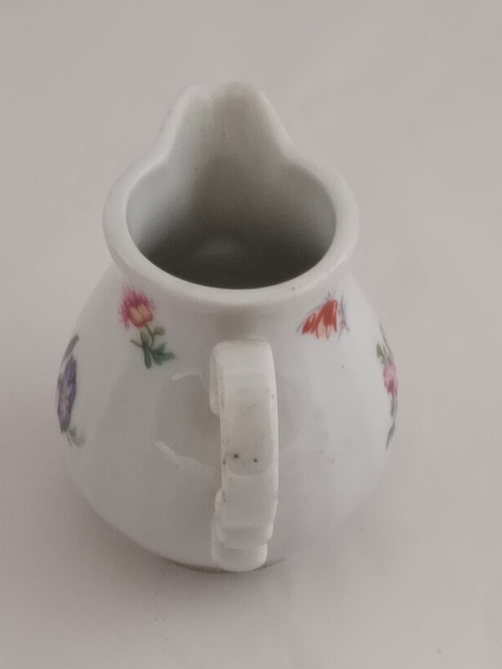 Rückansicht des Milchkännchens mit Fokus auf die glatte weiße Glasur und einzelne Blüten.