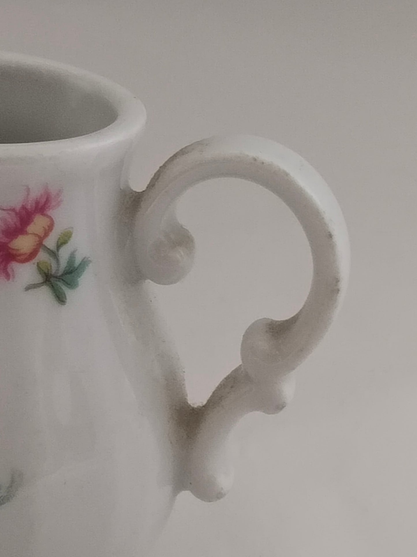 Detailaufnahme des kunstvoll geschwungenen Griffs eines Porzellan-Milchkännchens.