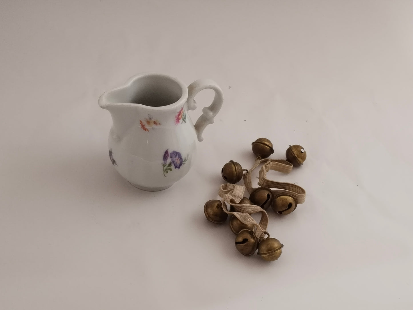 Porzellan-Milchkännchen fotografiert neben kleinen antiken Glocken als Dekoration.