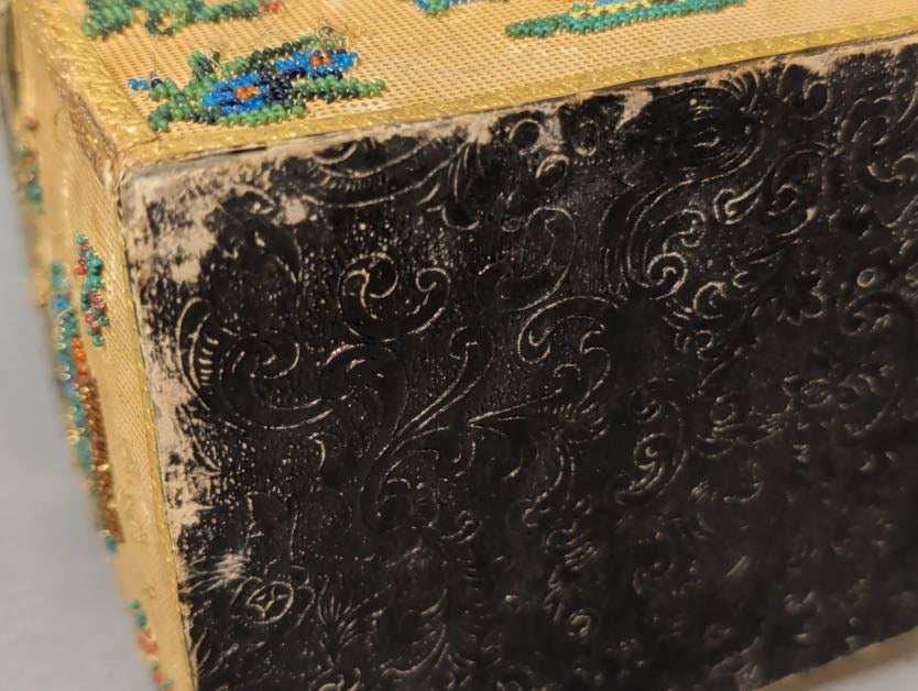 Nahaufnahme des Bodens: schwarzes geprägtes Papier mit Rocaille-Ranken, an den Kanten berieben und hell durchgescheuert