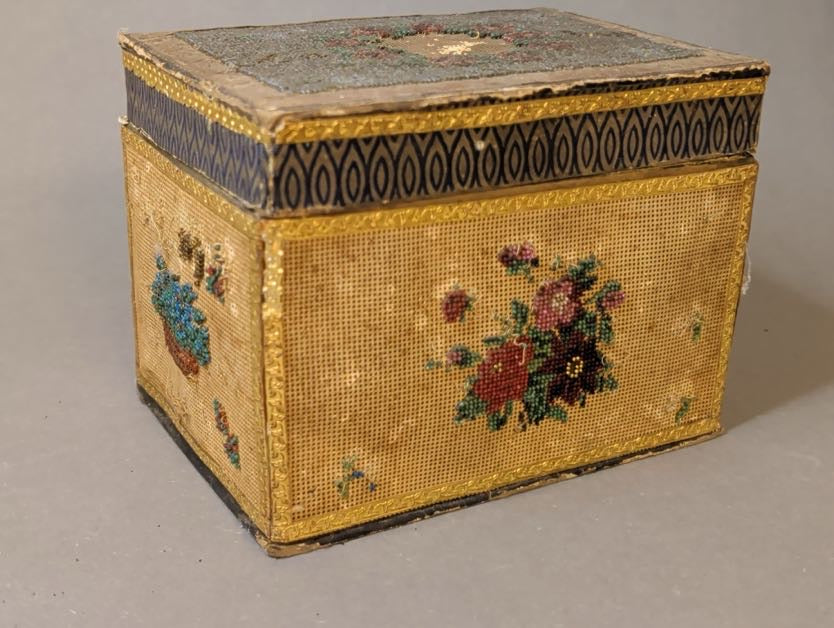 Längsseite des antiken Kästchens mit Rosenbouquet in Rot, Rosa und Violett aus Glasperlen, Deckelrand mit blauem Spitzbogenmuster