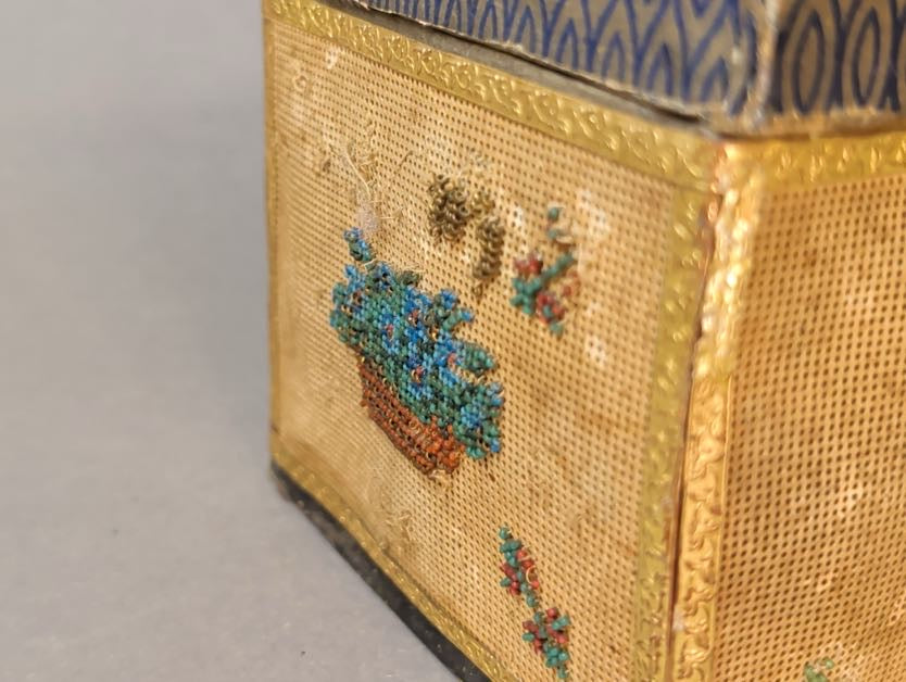Detail der Schmalseite: Körbchen mit blauen Glasperlen-Blüten auf Stickkarton, darüber Reste kleiner Perlmotive und lose Stickfäden