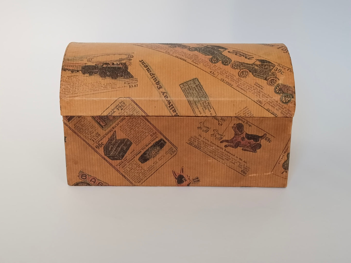 Handgefertigtes Schminkkästchen aus Karton mit gewölbtem Deckel, bezogen mit Vintage-Spielzeugkatalog-Papier, Frontansicht geschlossen

