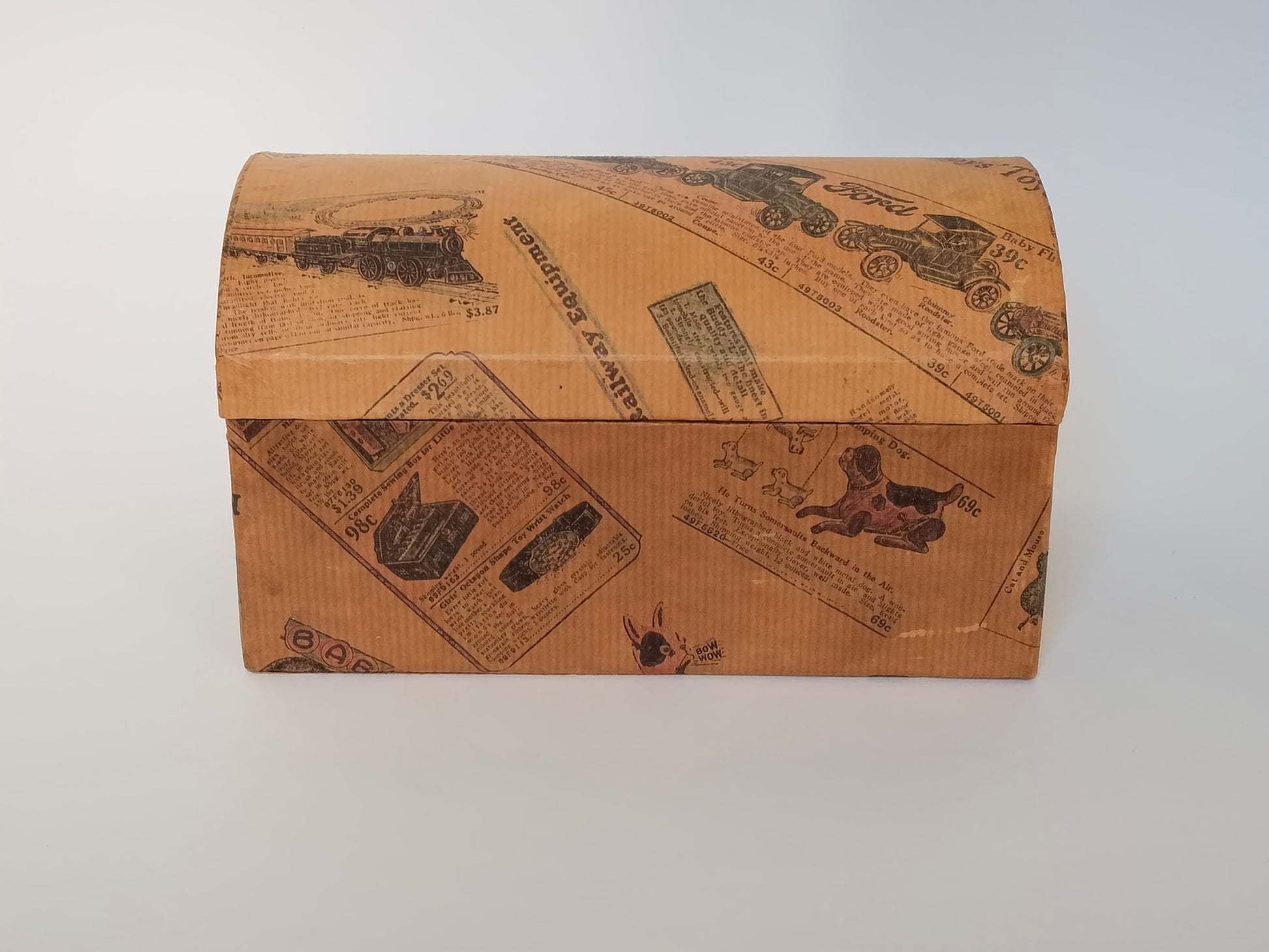Handgefertigtes Schminkkästchen aus Karton mit gewölbtem Deckel, bezogen mit Vintage-Spielzeugkatalog-Papier, Frontansicht geschlossen
