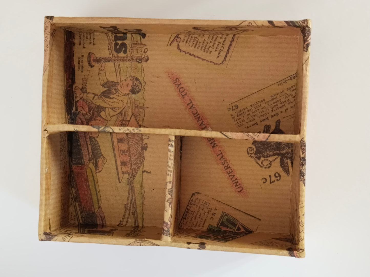 Herausnehmbarer Facheinsatz aus Karton von oben, innen mit Spielzeugkatalog-Papier ausgekleidet
