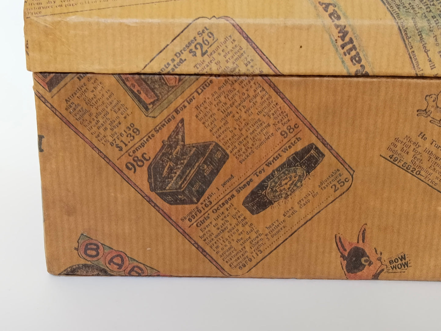 Detail der linken Vorderkante des Schminkkästchens: Papierbezug mit Nähkasten-Annonce und Spielzeug-Armbanduhr für 25 Cent