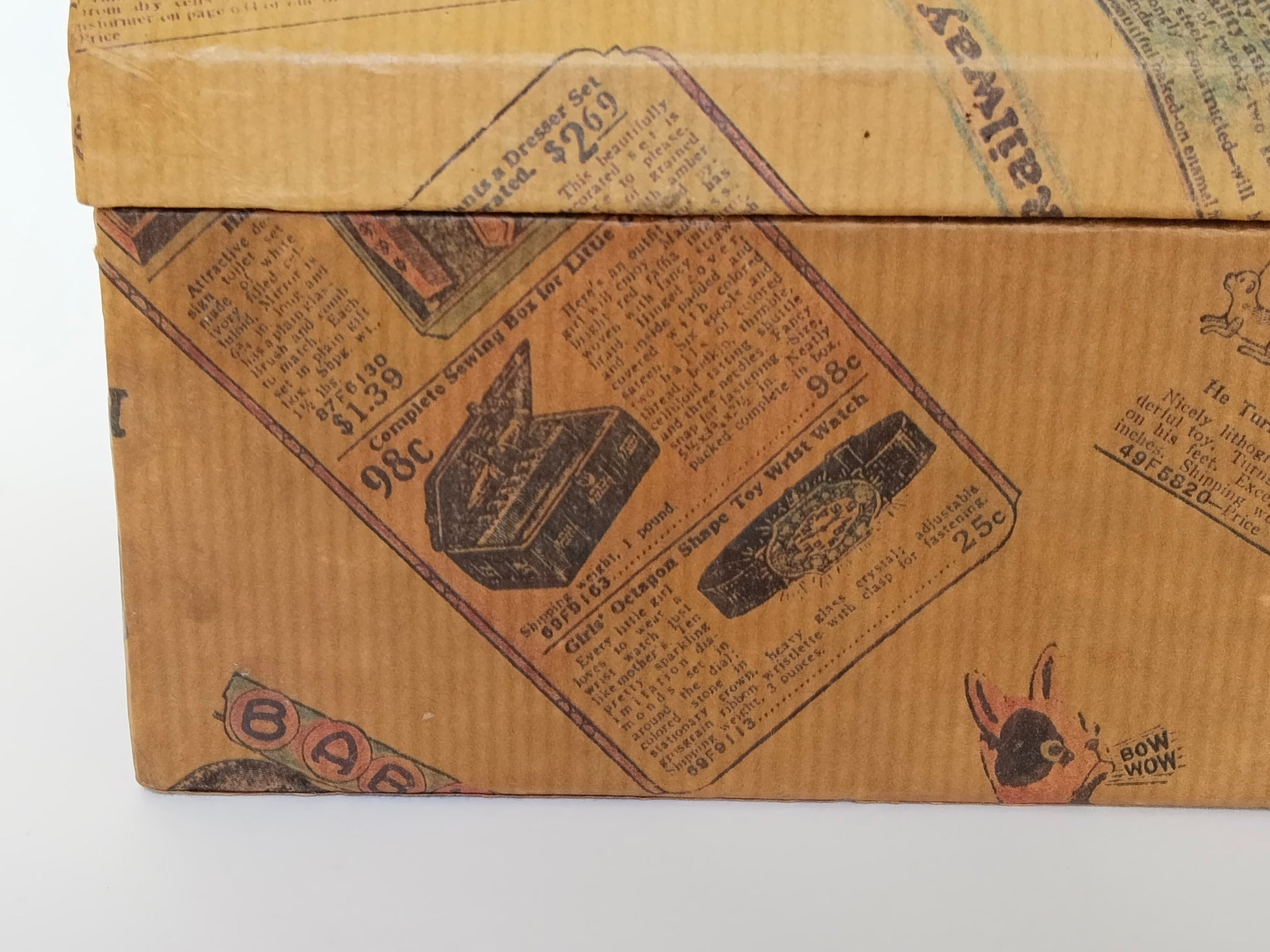 Detail der linken Vorderkante des Schminkkästchens: Papierbezug mit Nähkasten-Annonce und Spielzeug-Armbanduhr für 25 Cent