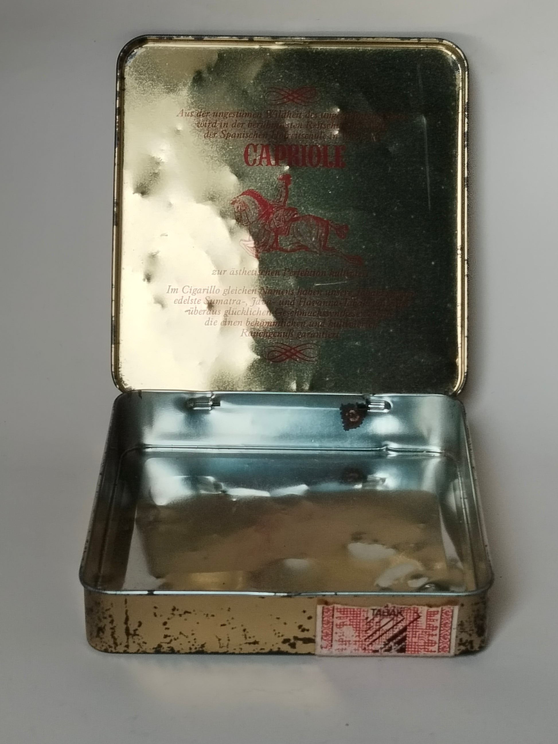 Geöffnete Capriole-Zigarillodose mit goldfarbenem Werbetext im Deckel